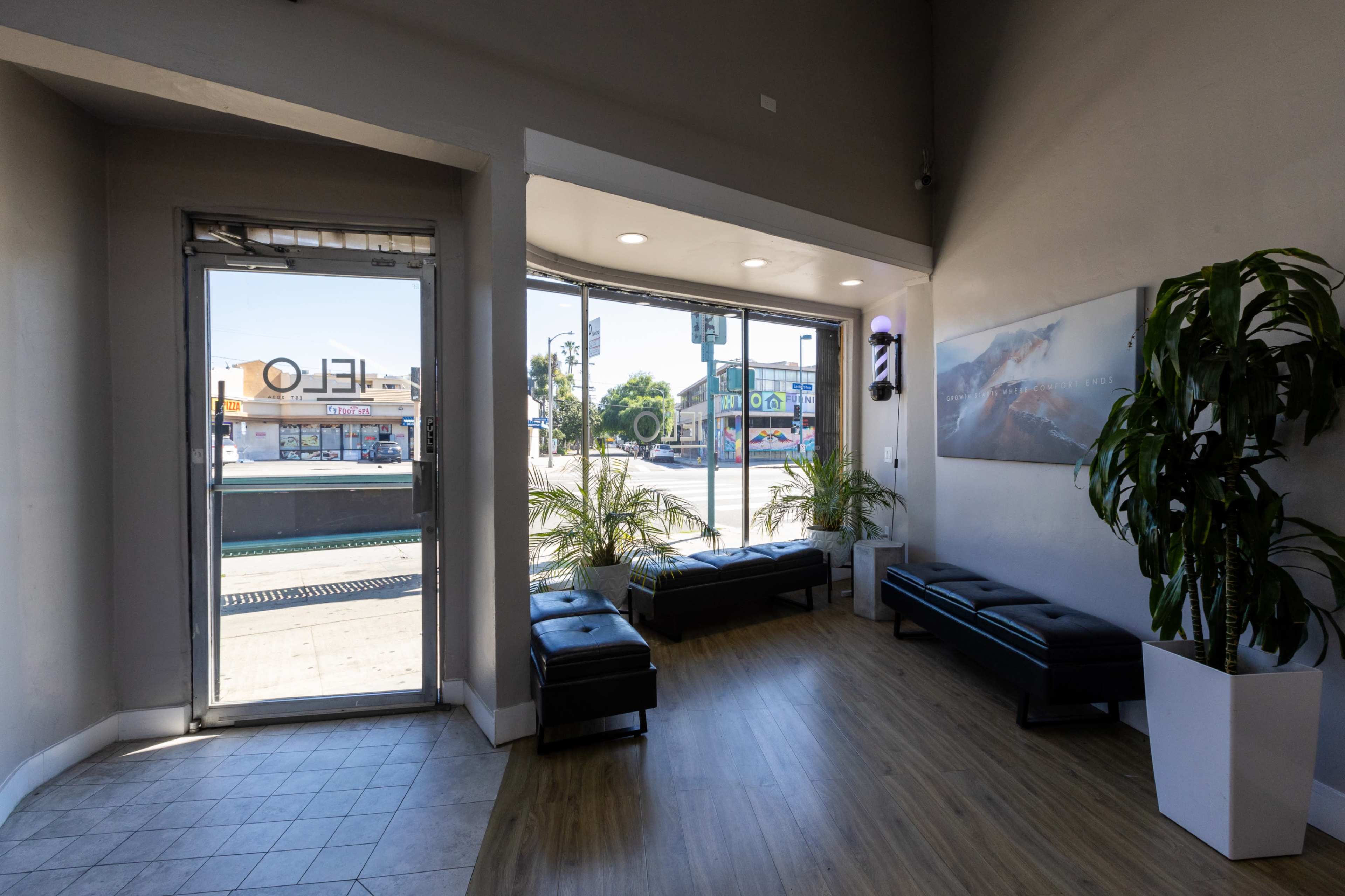 The image shows a modern waiting area with two benches, a decorative plant, and a large window overlooking the street.