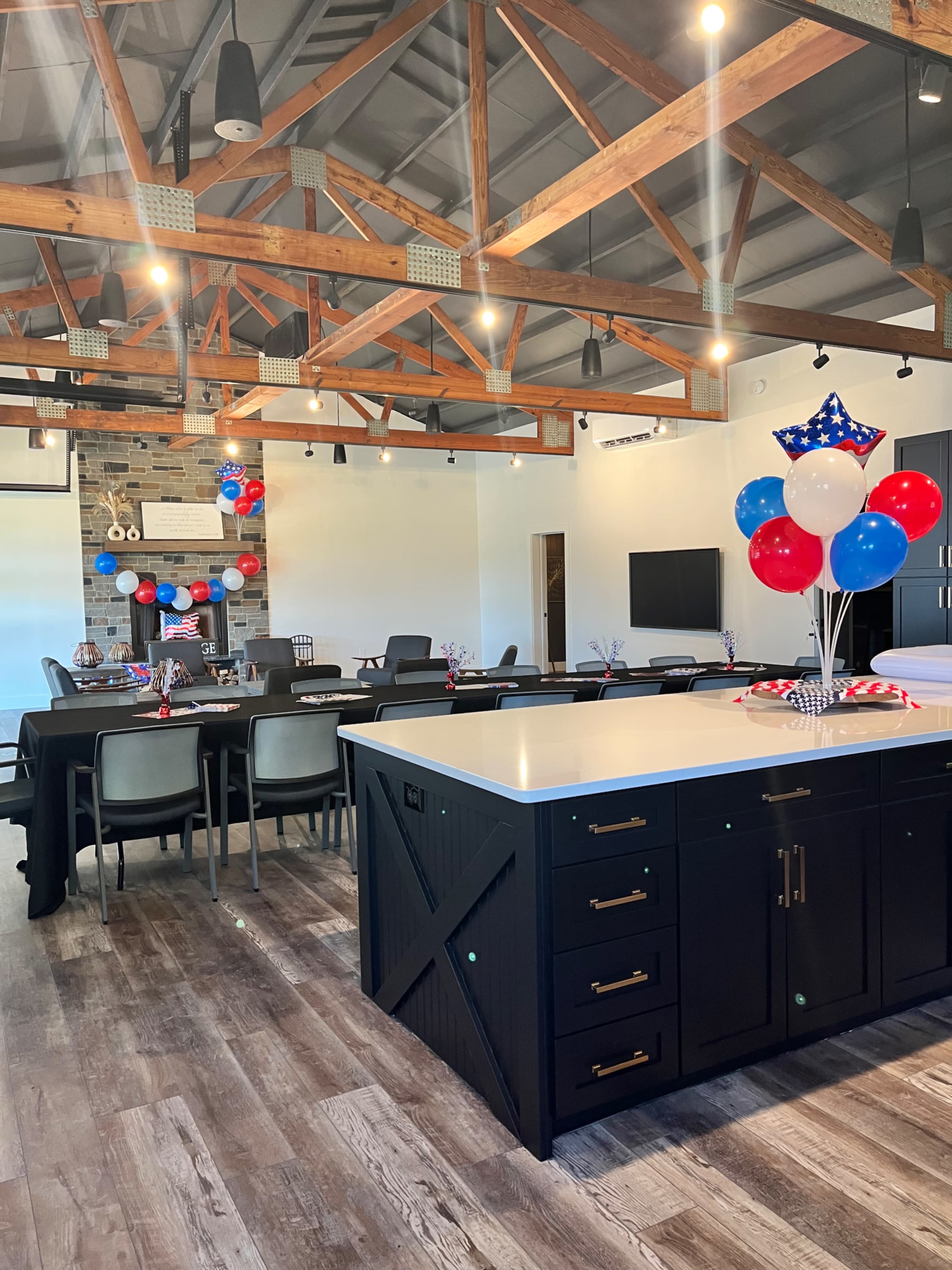 A modern meeting room features a large central island, seating arrangements, and patriotic decorations of red, white, and blue balloons.