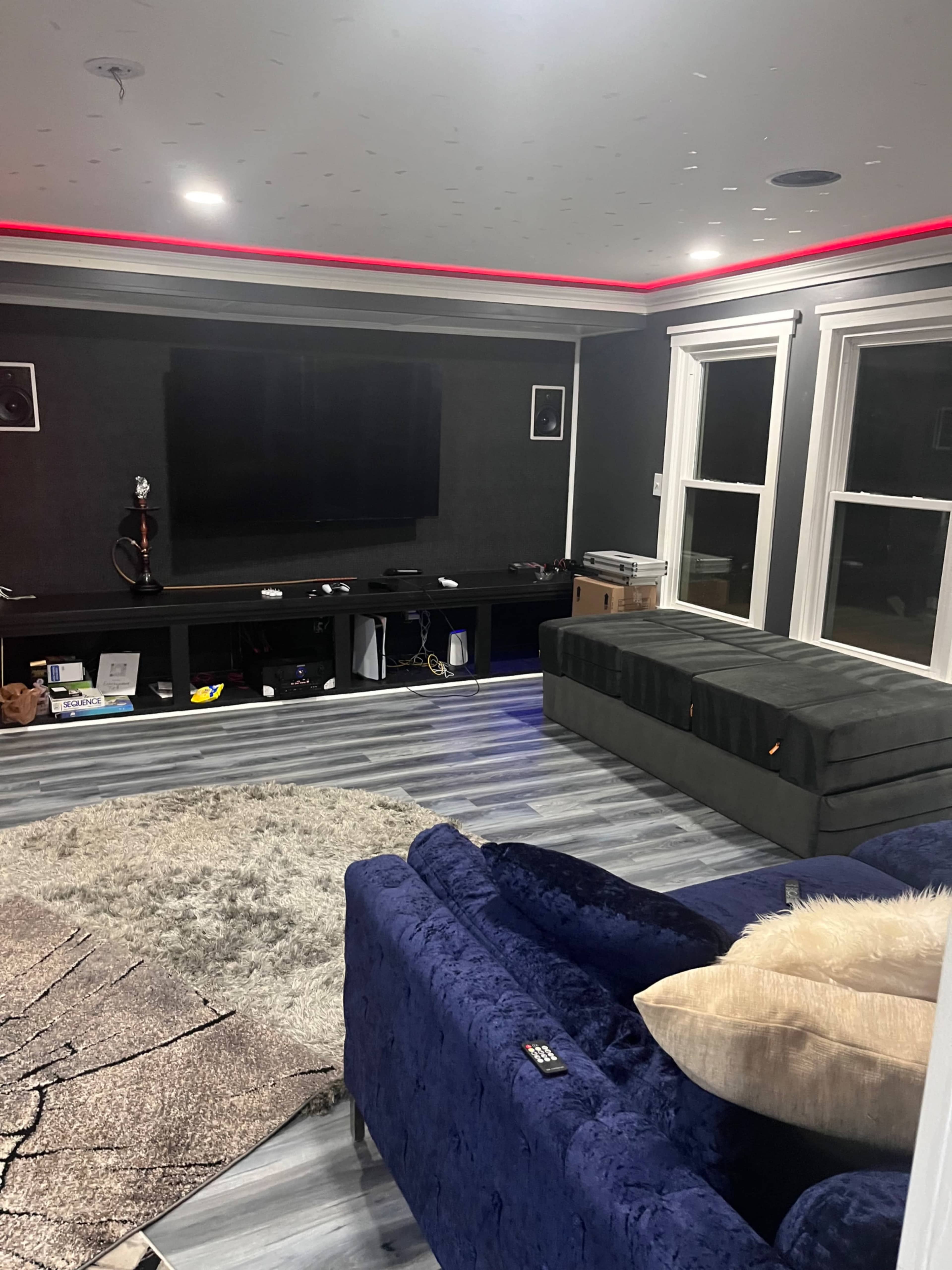 A modern living room with a dark gray wall, a television mounted on the wall, a green velvet sofa, and a gray area rug on the floor.