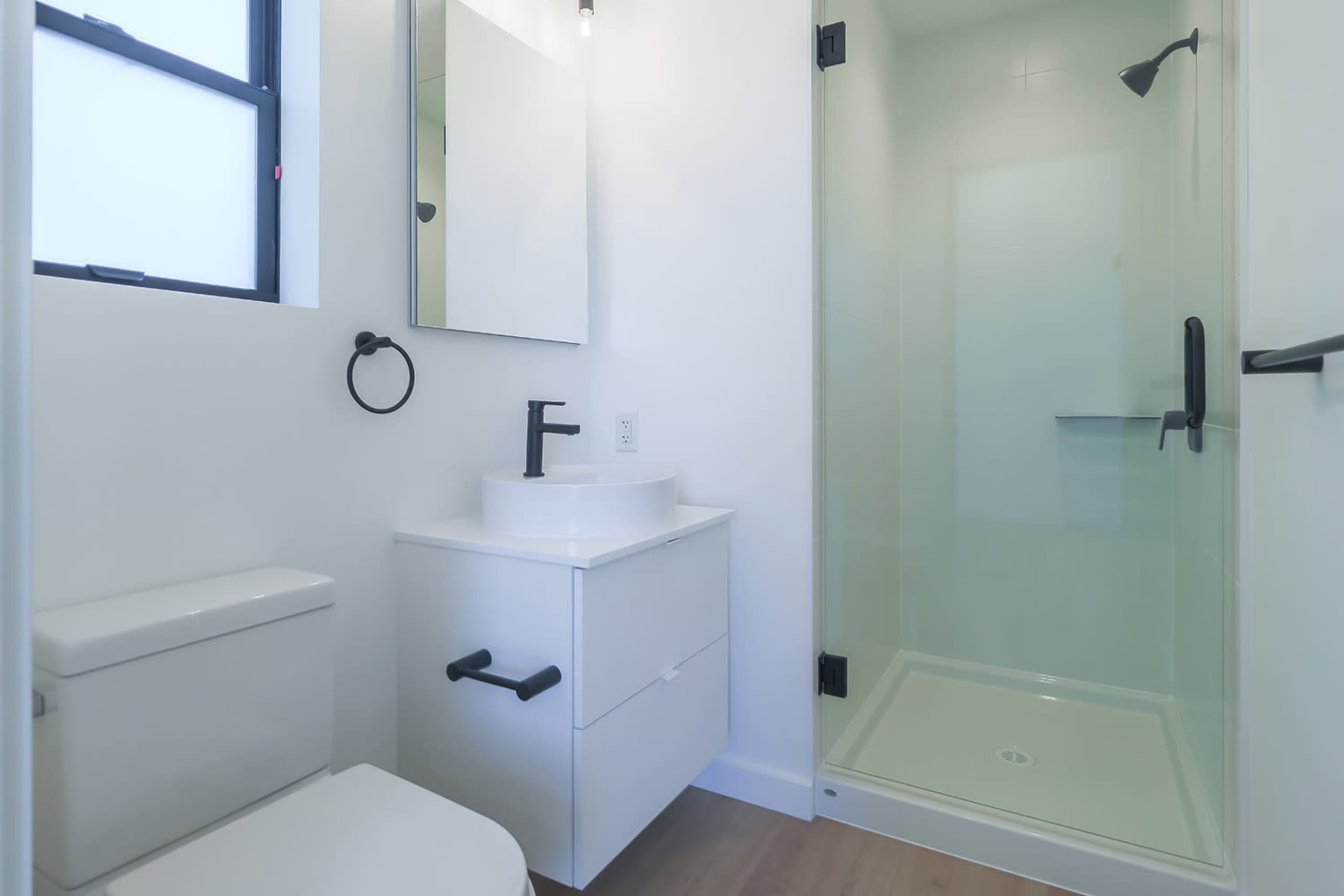 A modern bathroom featuring a toilet, a sink with a mirror above it, and a glass shower enclosure.