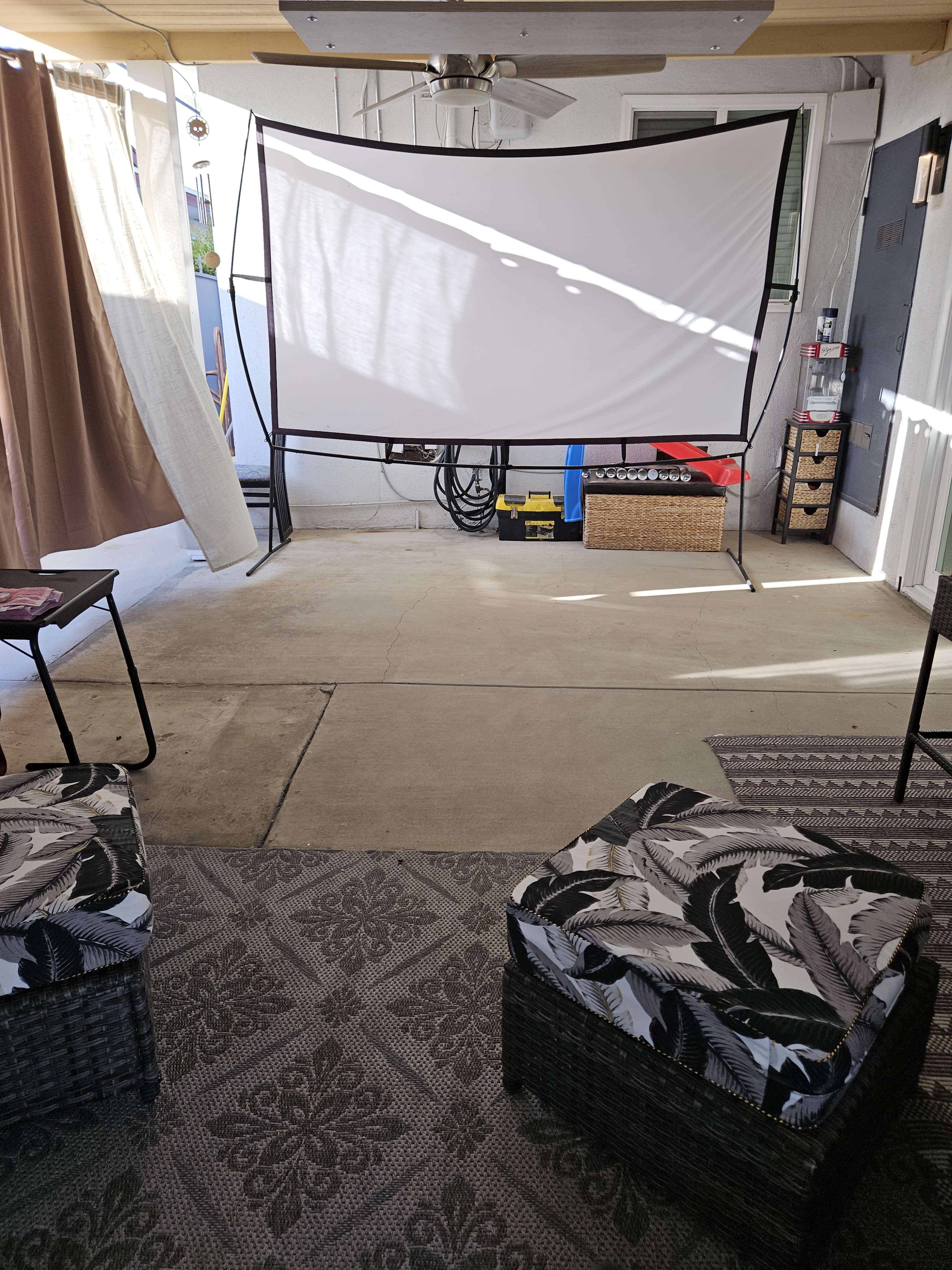 A screened area with a large white projector screen set up in the center, flanked by two cushioned stools on a patterned rug.