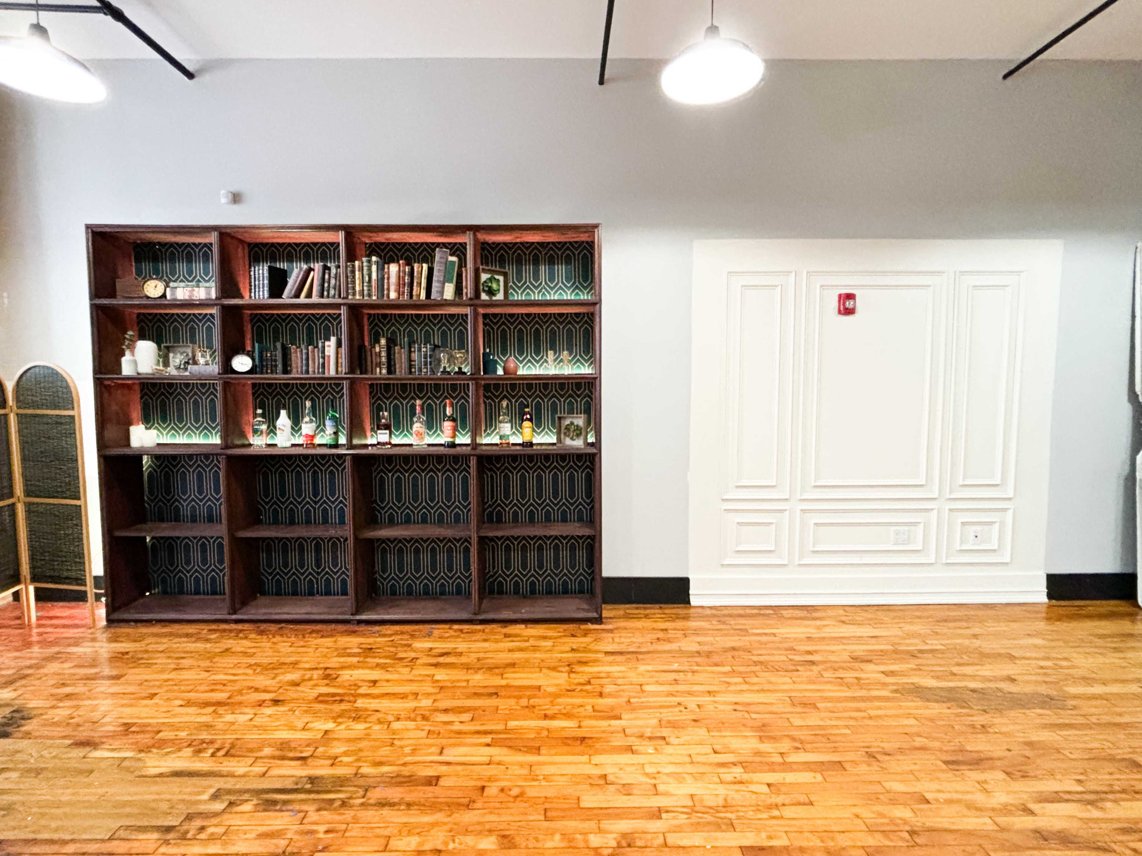 A wooden bookshelf filled with decorative items and books against a neutral wall, with polished wooden flooring visible in the foreground.