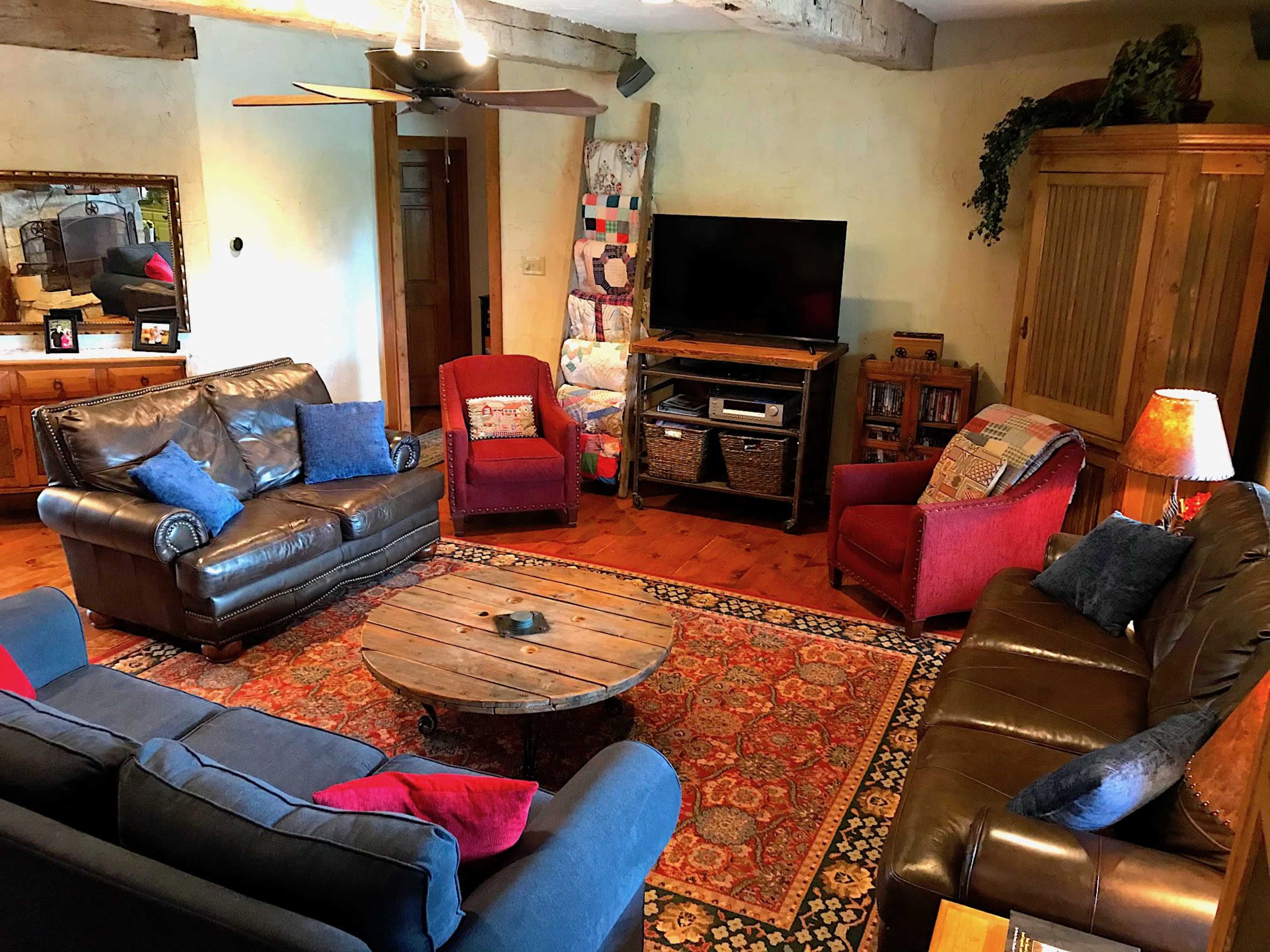 A rustic living room features a mix of leather sofas, upholstered chairs, a wooden coffee table, and a television surrounded by decorative furnishings.