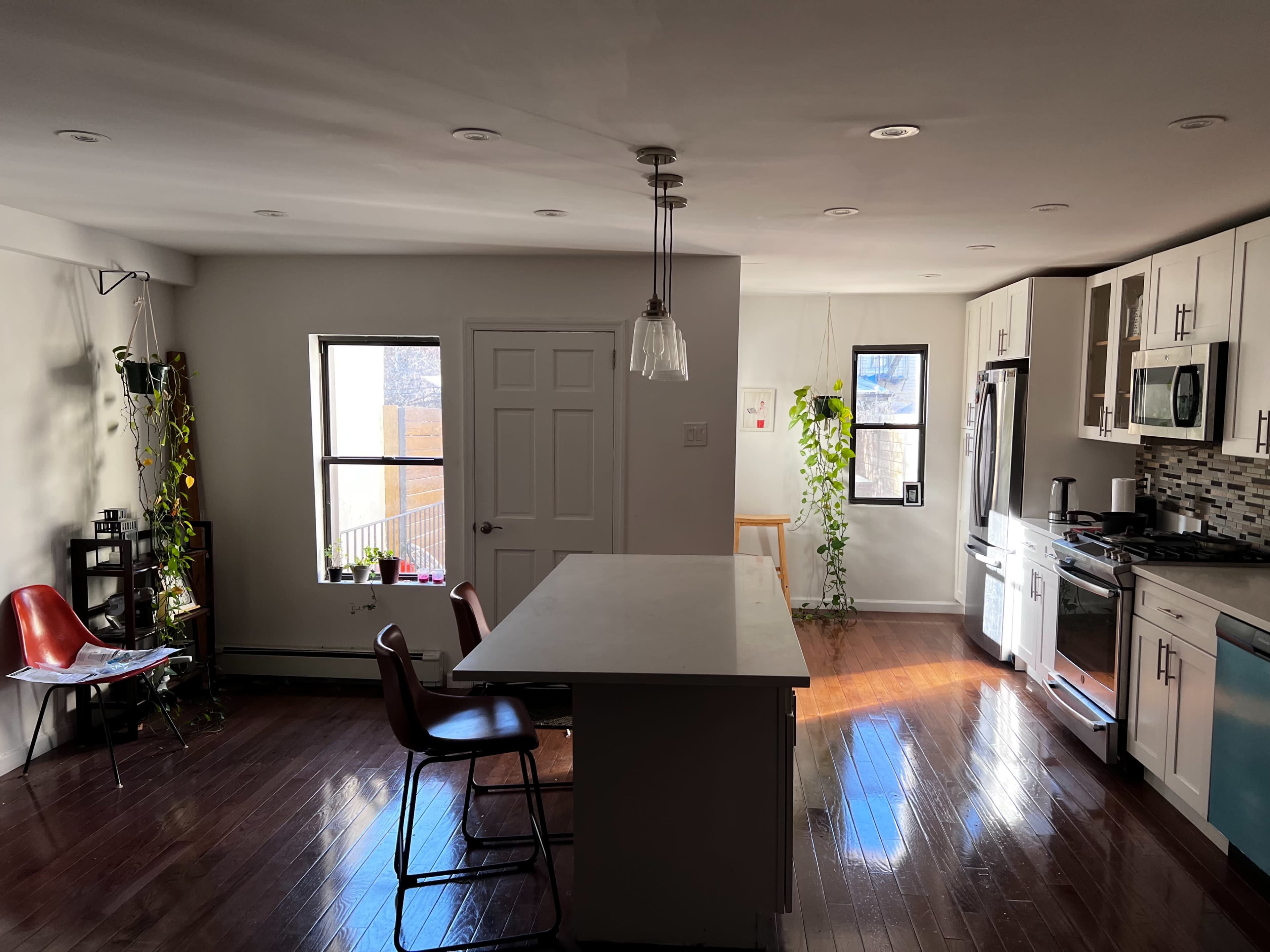 A spacious kitchen features an island with stools, white cabinetry, and large windows allowing natural light to fill the room.