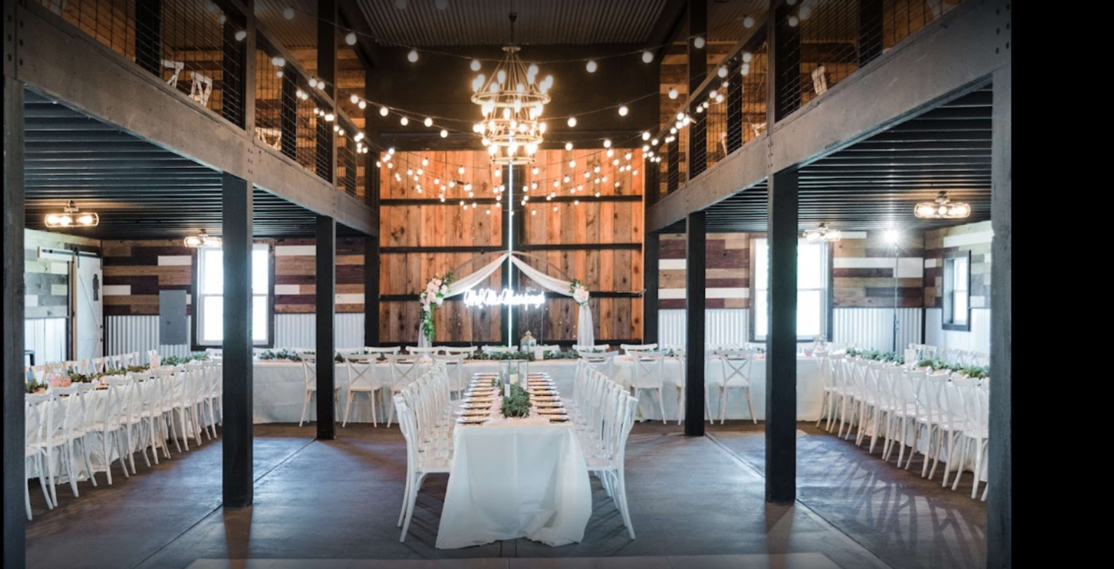 A decorated indoor venue with long tables set for a formal event, featuring string lights and a central chandelier.