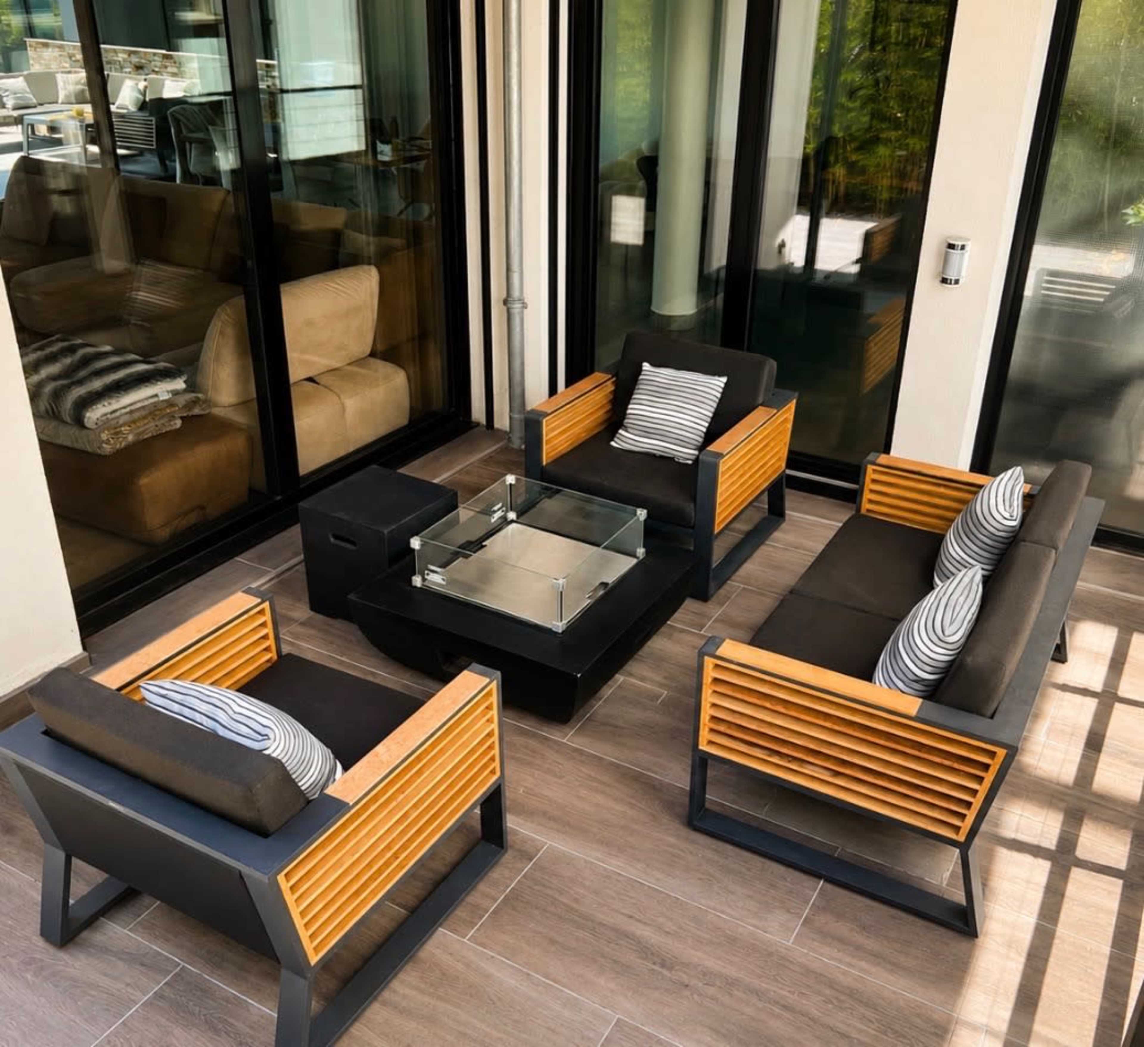 The image shows a modern outdoor seating area with four armchairs, a small table, and large glass doors leading to an indoor space.