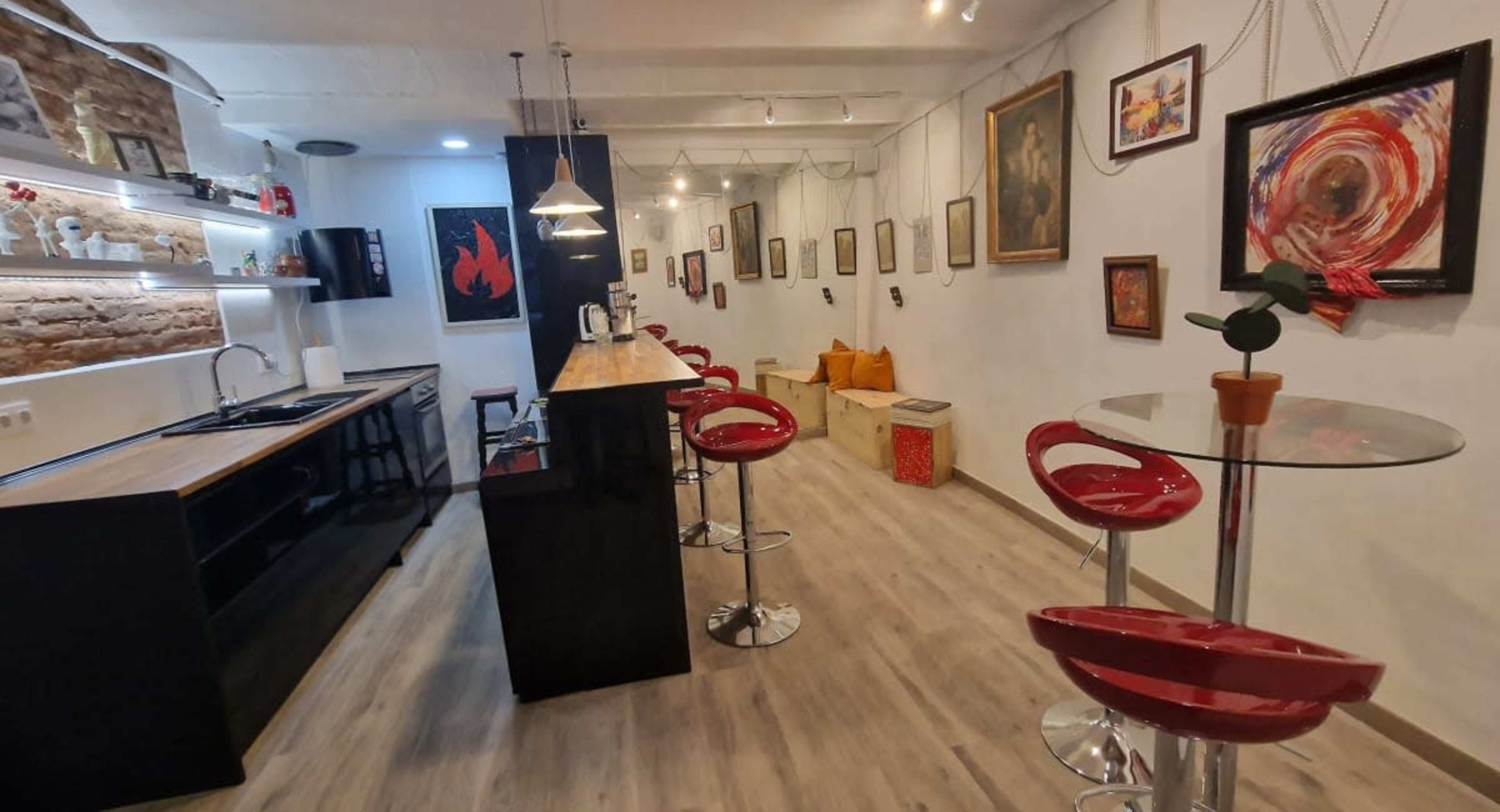 A modern kitchen and dining area with red bar stools, a glass table, and various framed artworks on the walls.