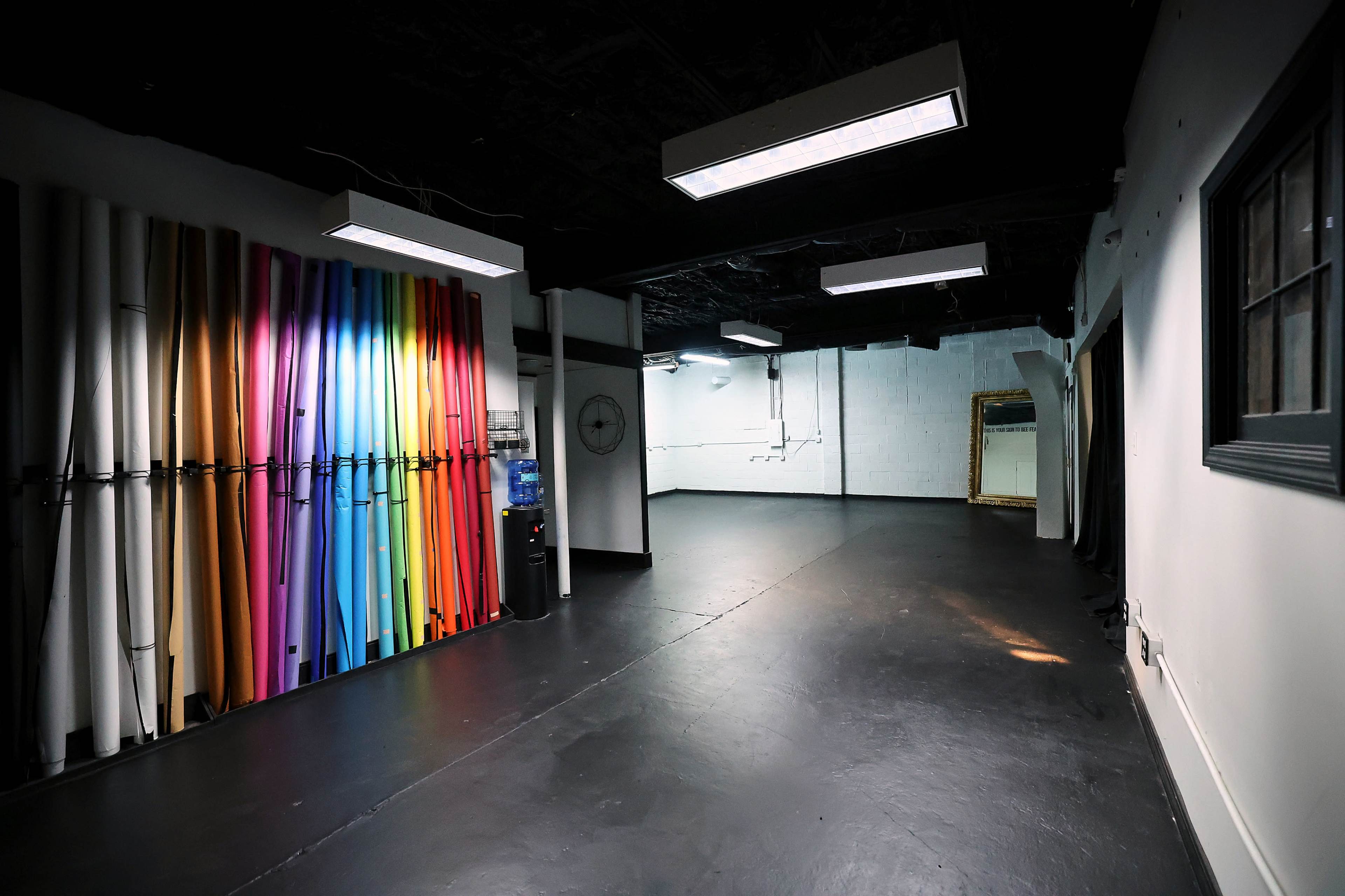 The image shows a spacious studio with vibrant colored backdrops arranged against one wall and plain, white walls on the opposite side.