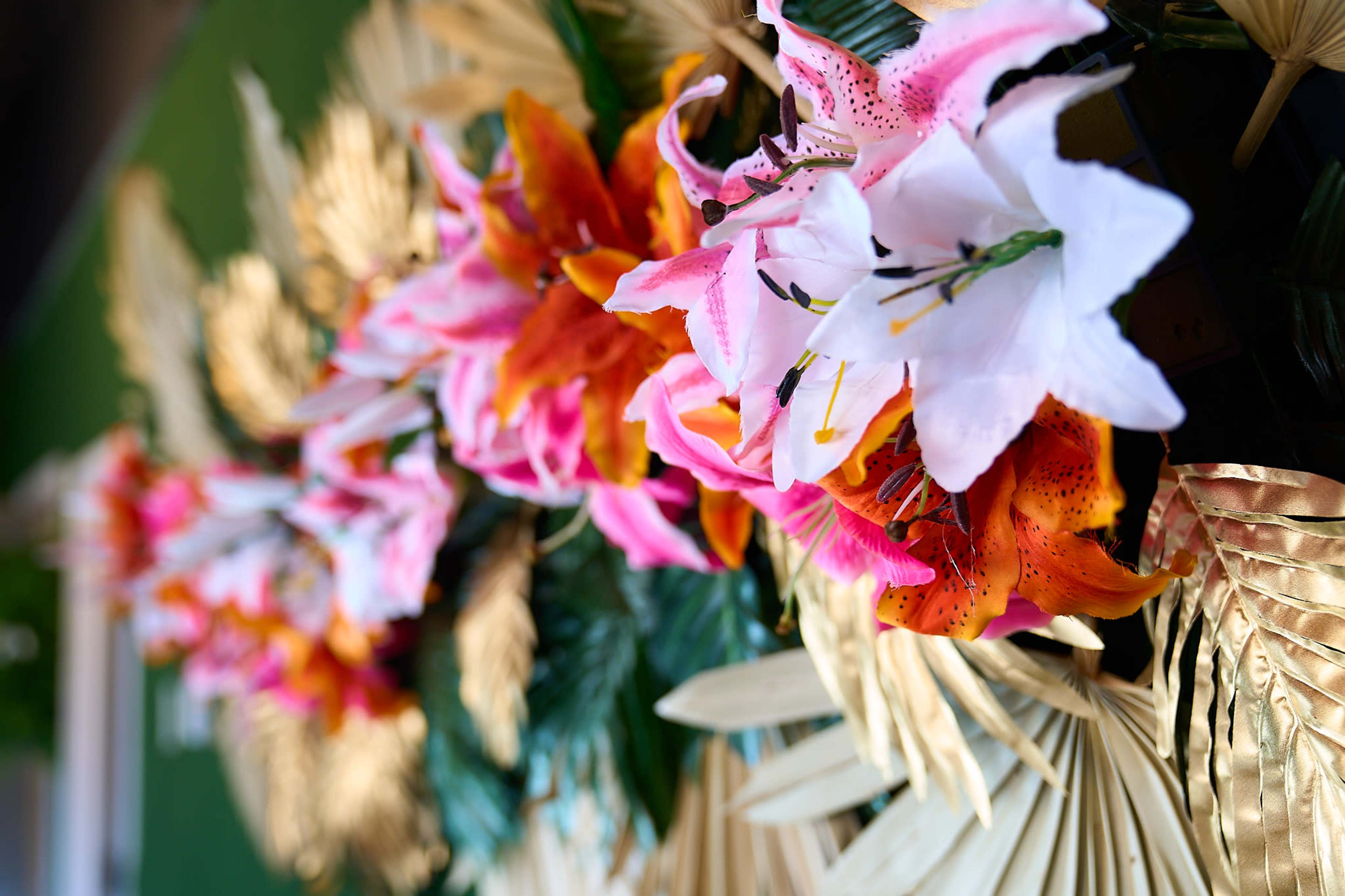 A decorative arrangement of vibrant artificial flowers and golden leaves against a green background.