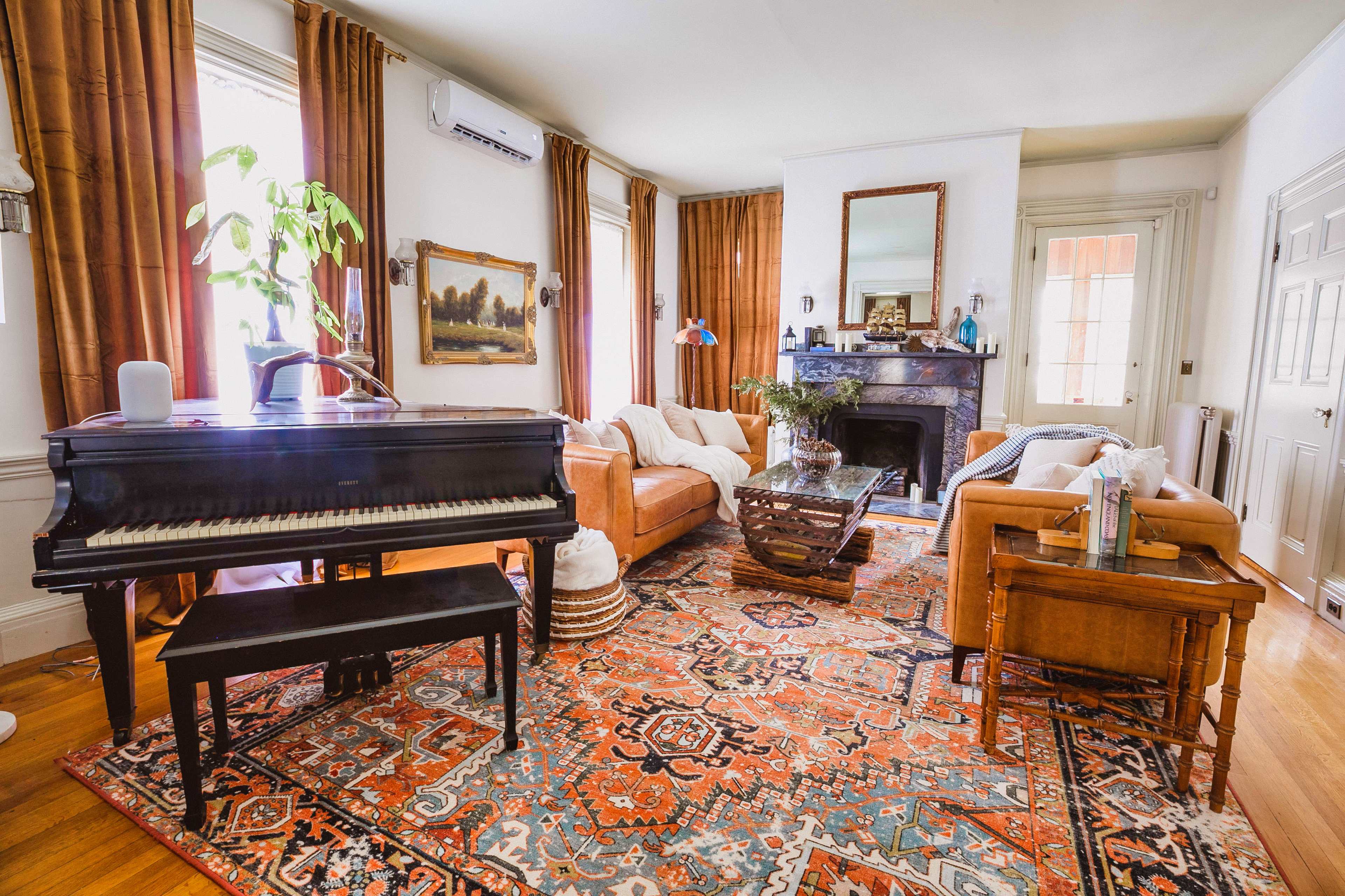 A spacious living room features a black piano, two brown sofas, and a decorative coffee table on a colorful area rug.