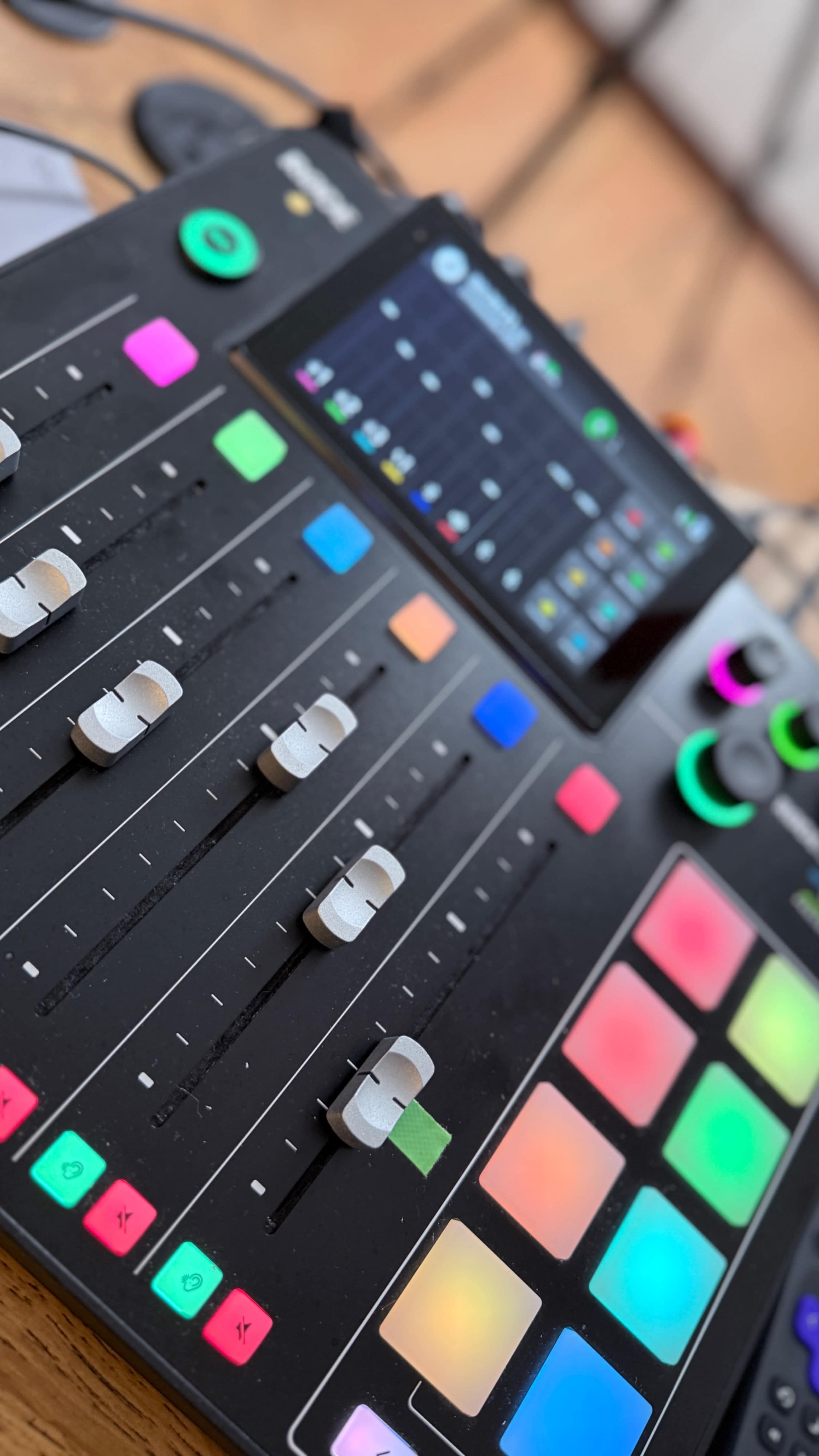 A close-up view of a music production controller featuring faders, colorful pads, and a digital display.