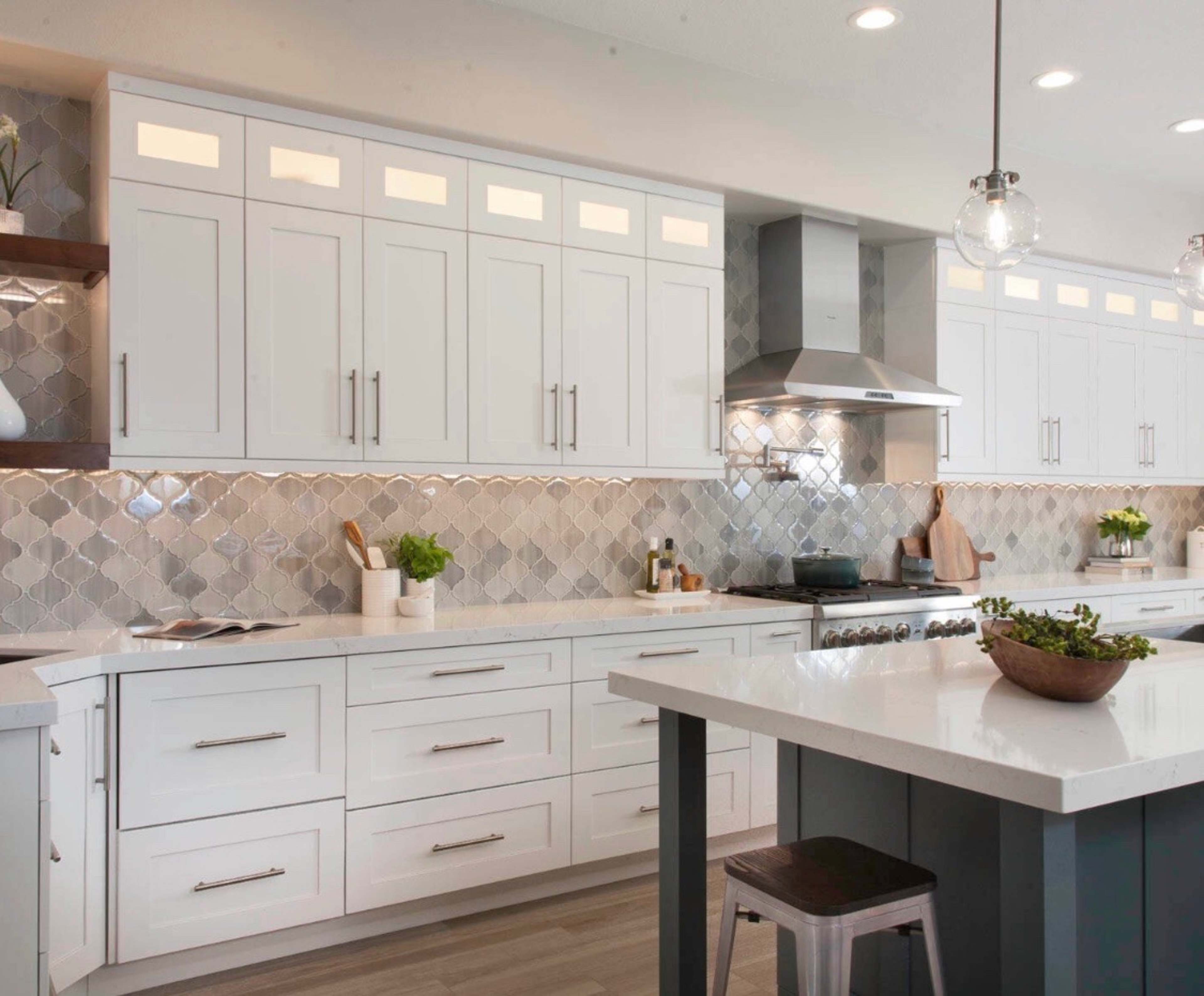 The image shows a modern kitchen with white cabinetry, a stainless steel range hood, and a herringbone tile backsplash.