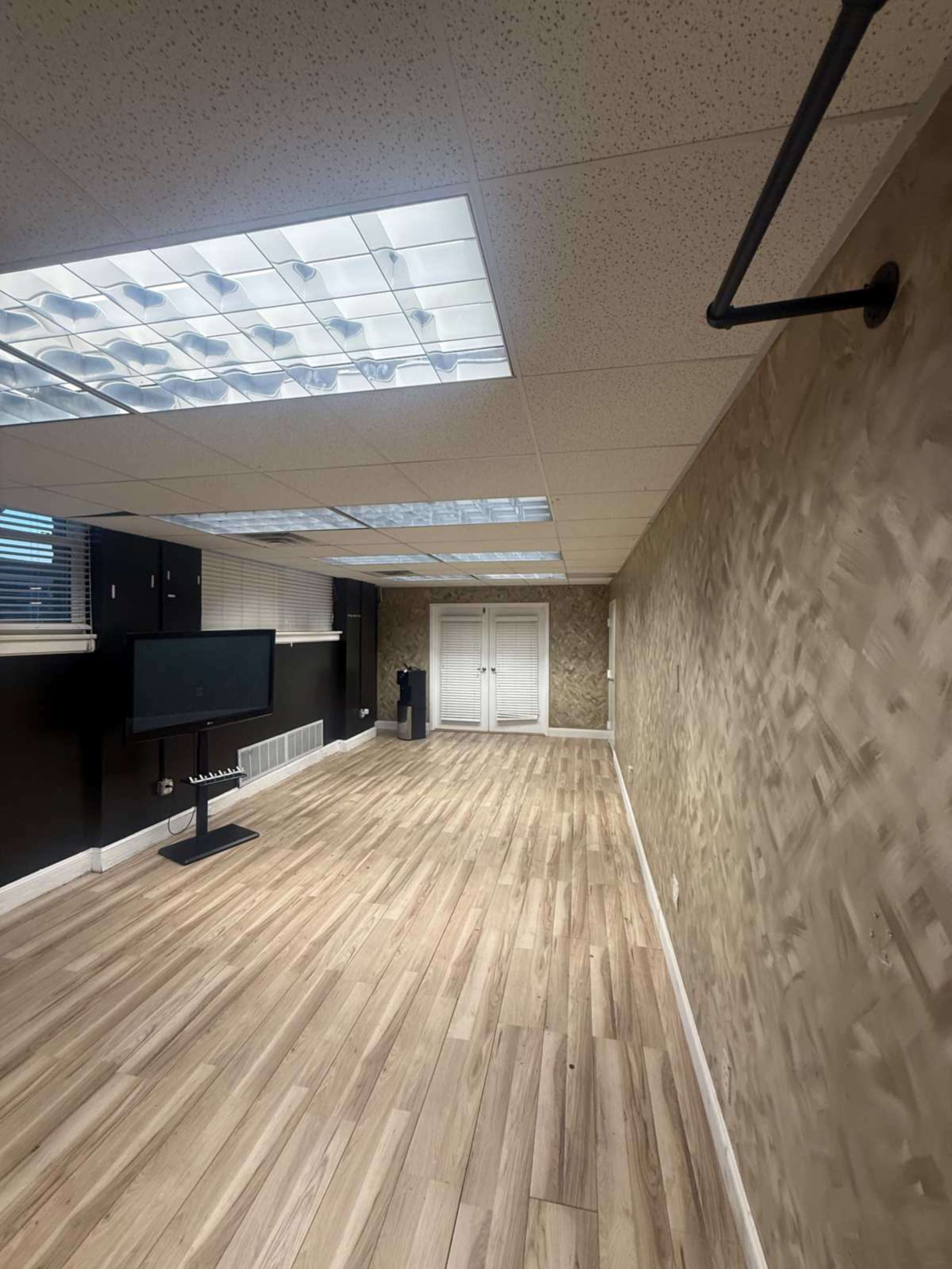The image shows a spacious, well-lit room with light wood flooring, a TV on a stand, and a closet with double doors at the far end.