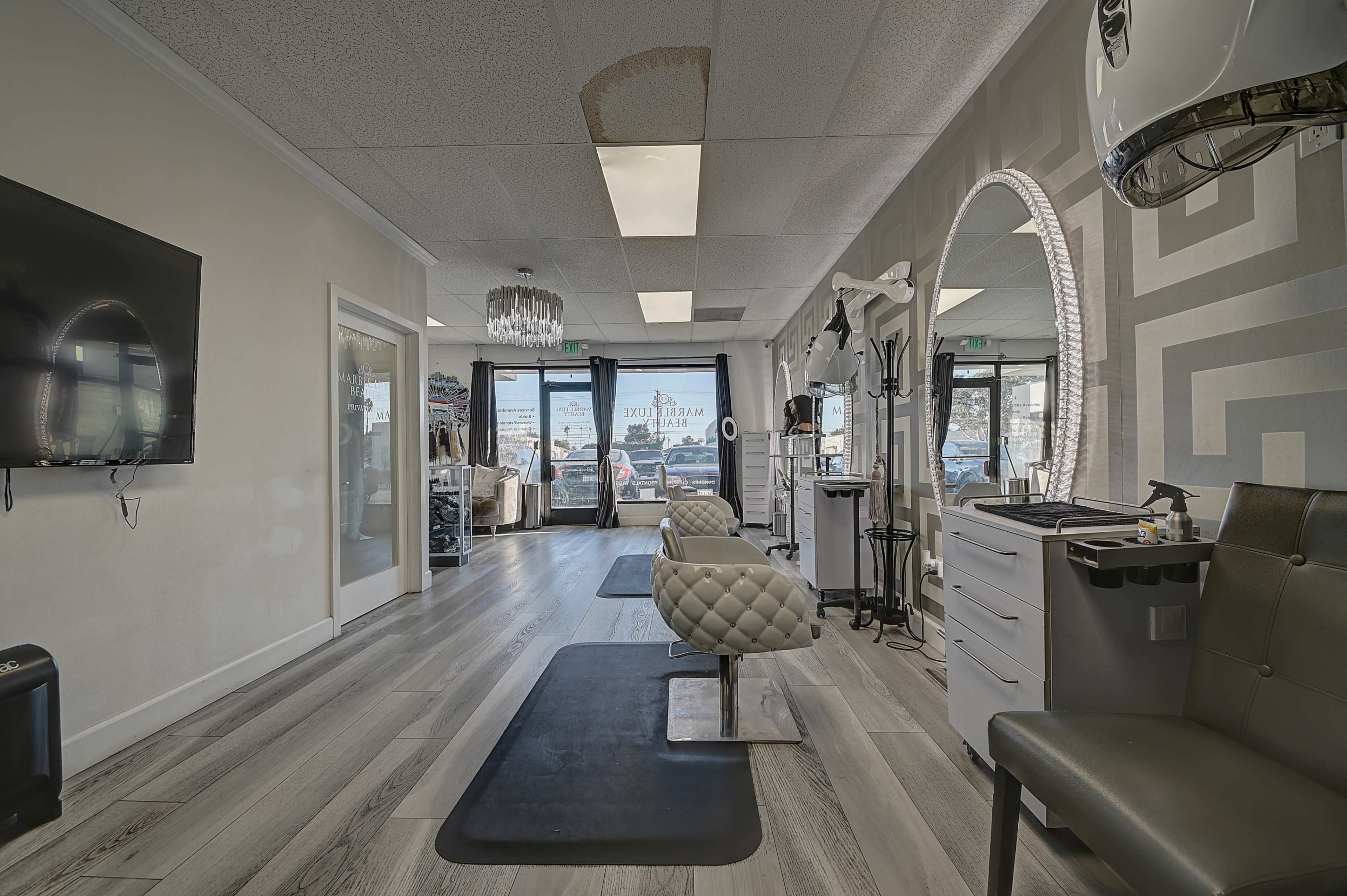 A modern salon interior with styling stations, a large circular mirror, and a waiting area, featuring light-colored walls and wooden flooring.