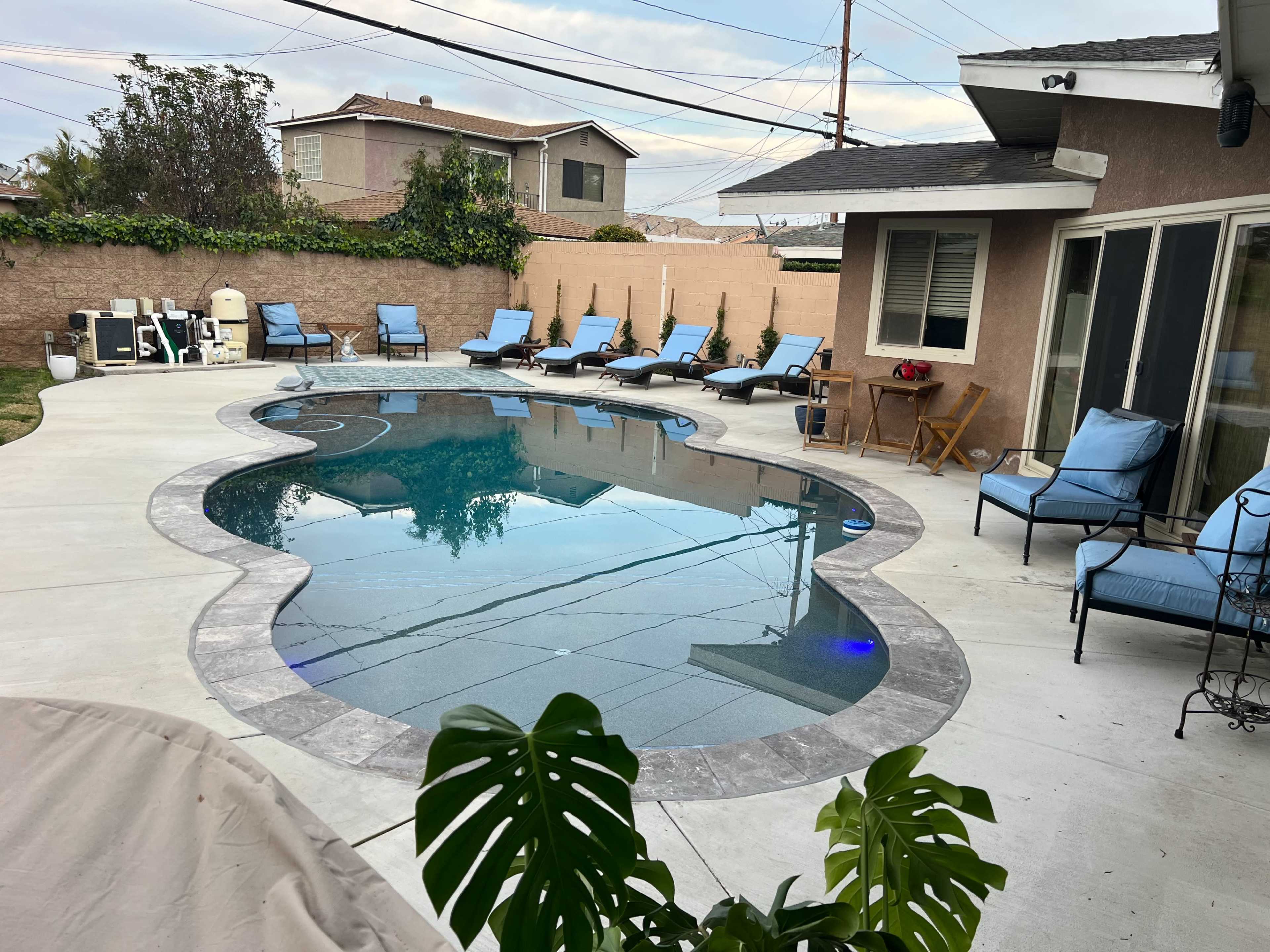 A residential backyard with a kidney-shaped swimming pool surrounded by lounge chairs and a small outdoor seating area.