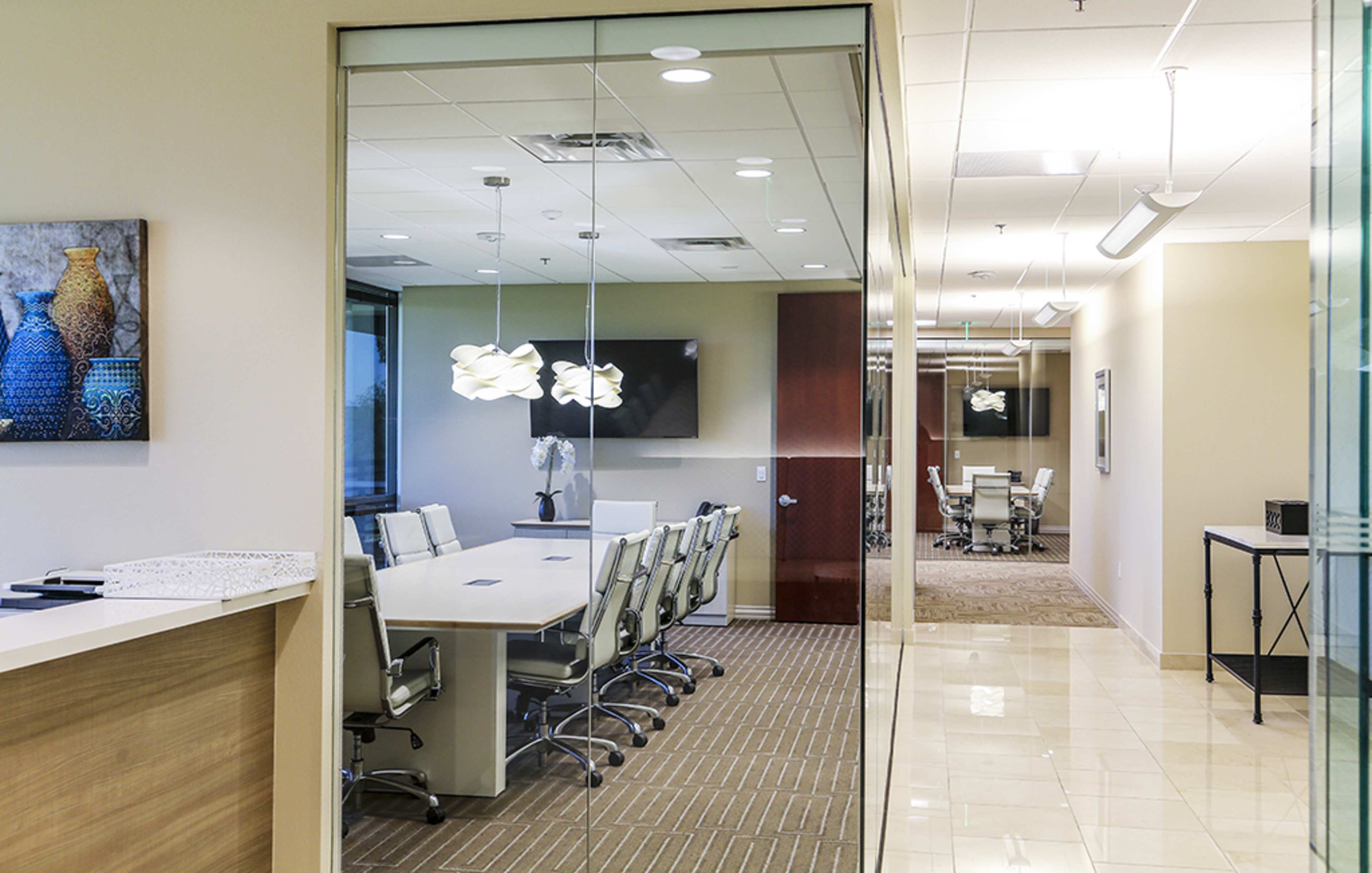 The image shows a modern office environment featuring a conference room with a long table and ergonomic chairs, visible through glass walls.