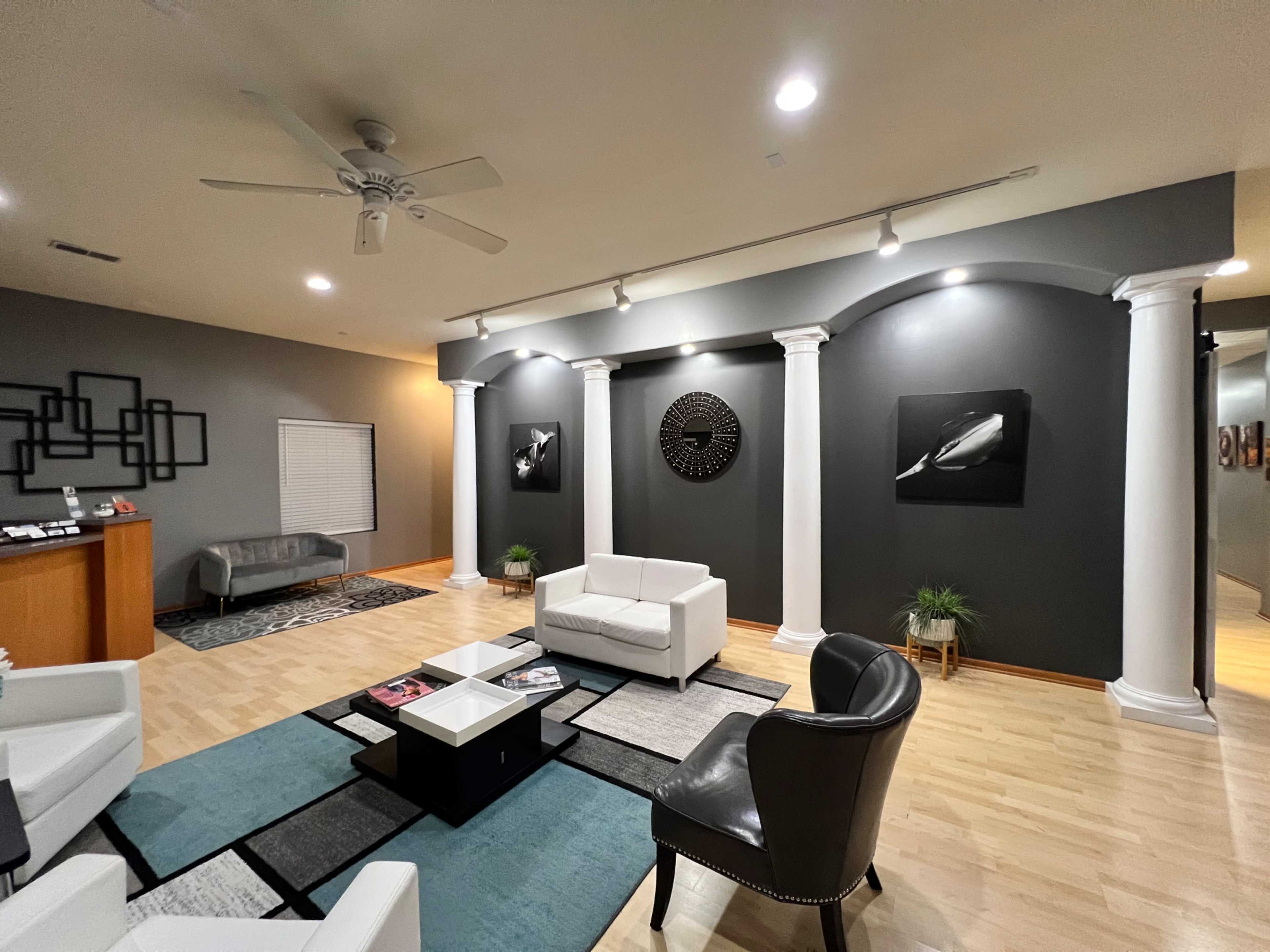 The image shows a modern living room with two white sofas and a dark gray wall featuring decorative columns and framed black-and-white artwork.
