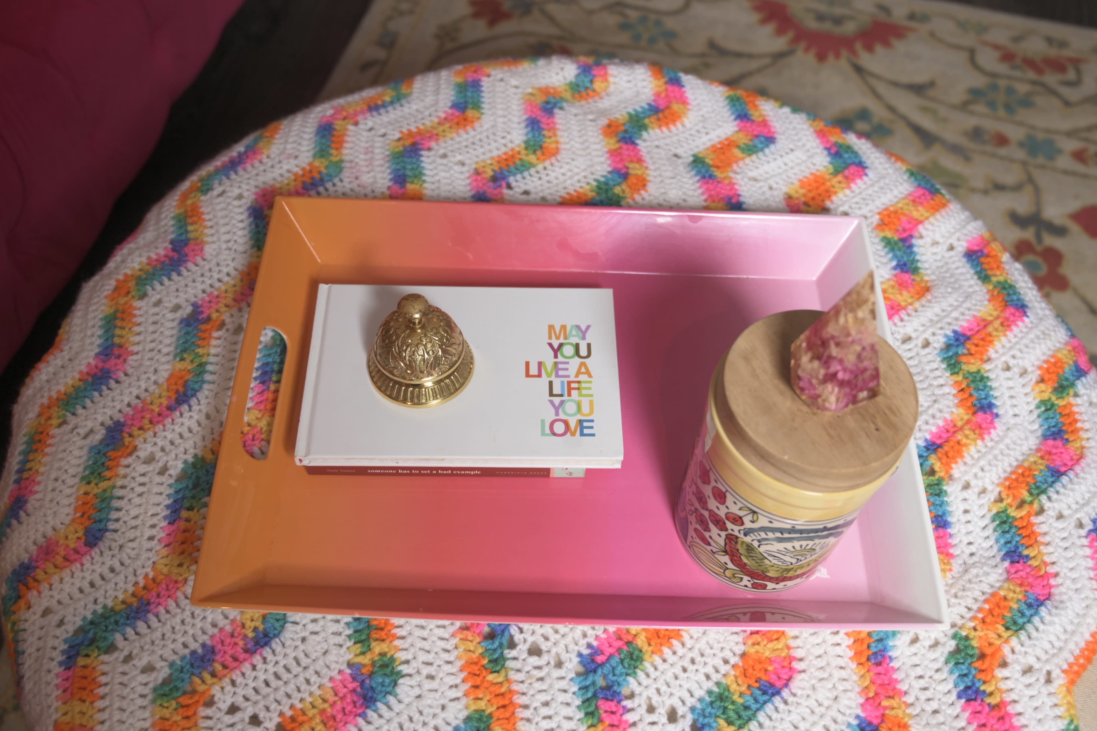 A colorful tray holds a decorative gold object, a candle jar, and a card that says "May you live a life you love."