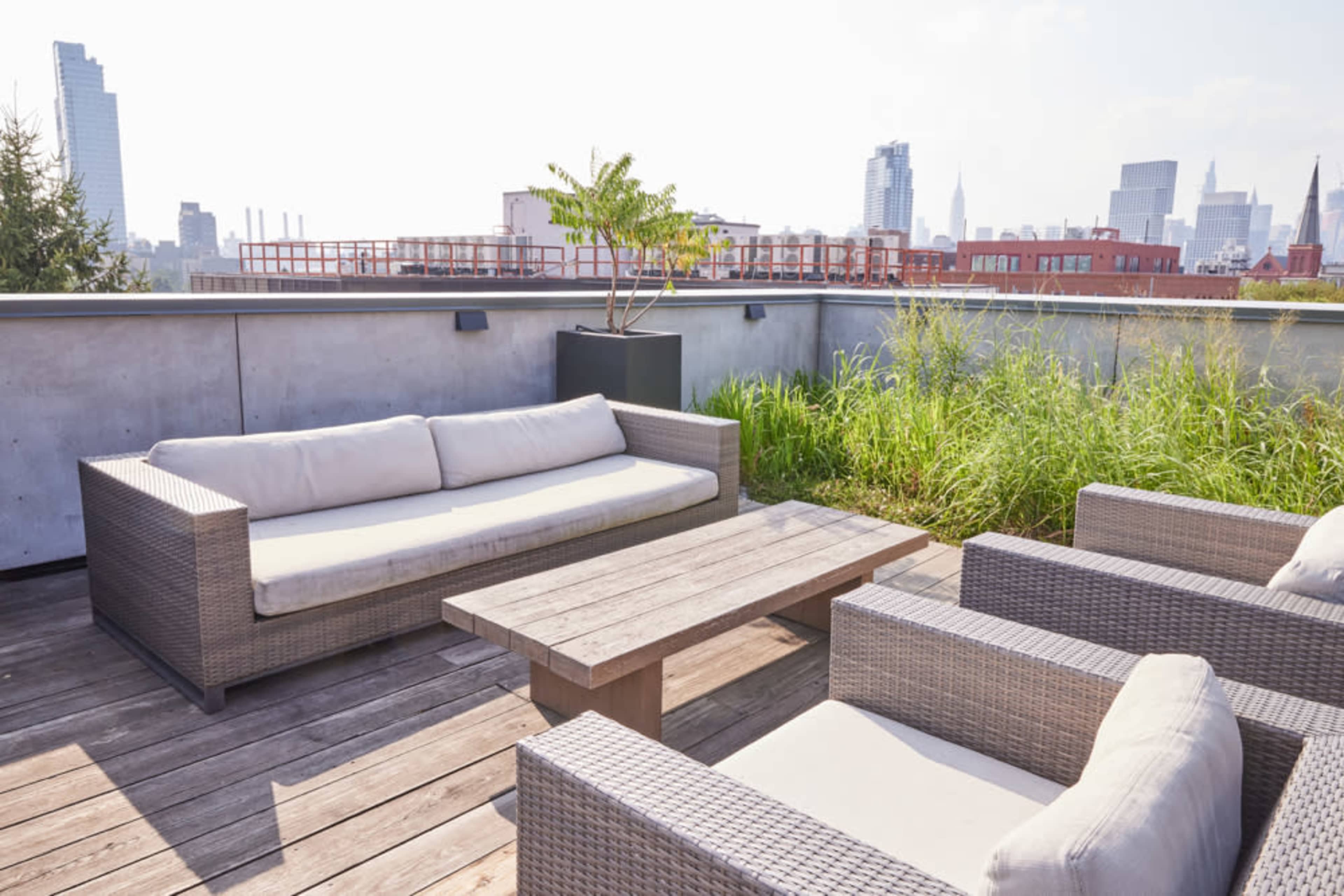 A rooftop terrace features a wooden table surrounded by wicker seating and overlooks a city skyline.