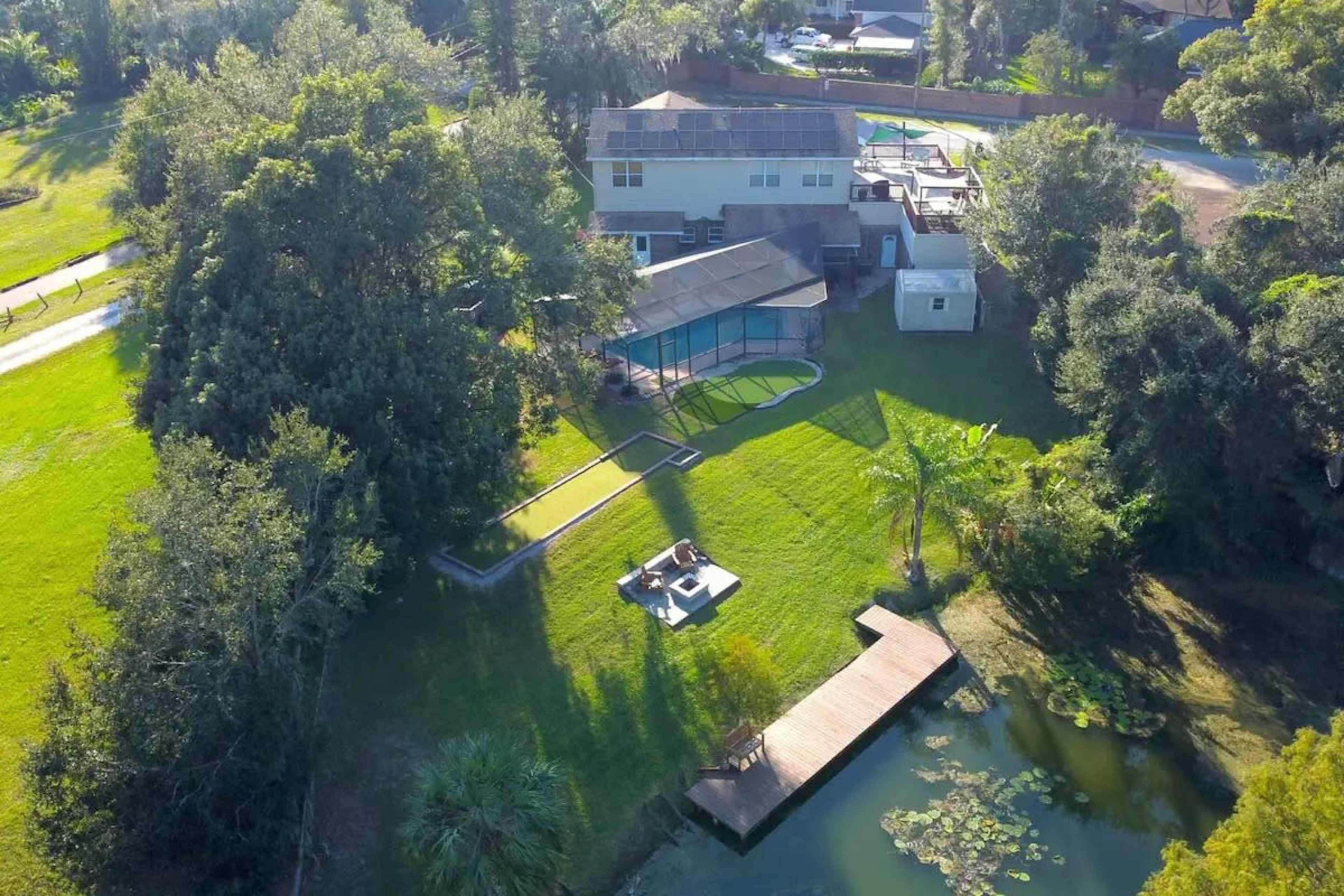The image shows an aerial view of a property featuring a large house, a swimming pool, and a pond surrounded by greenery.