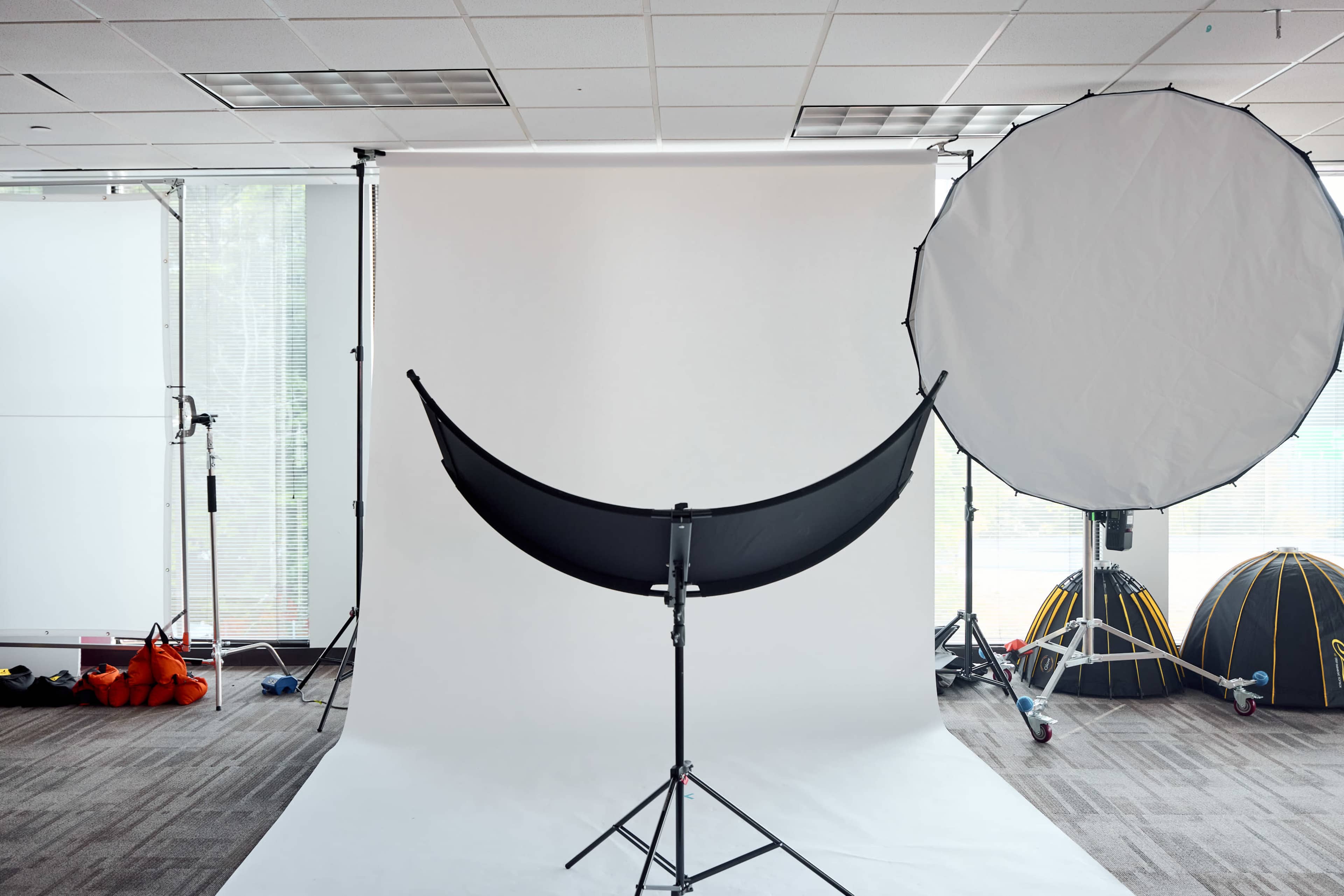 The image shows a photography studio setup with a backdrop, lighting equipment, and a large umbrella reflector.