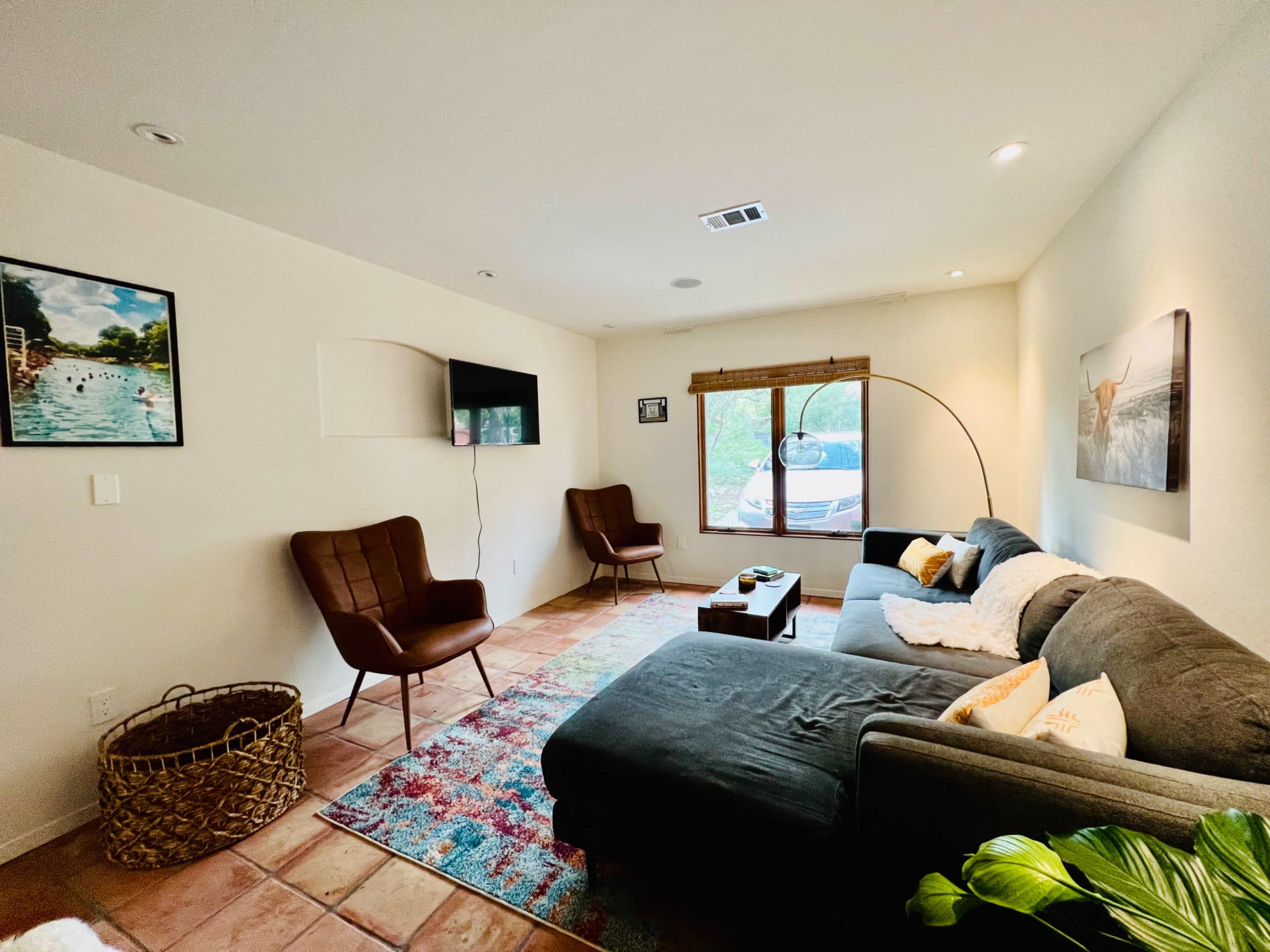 The living room features a sectional couch, two chairs, a round coffee table, and a large window with a view.