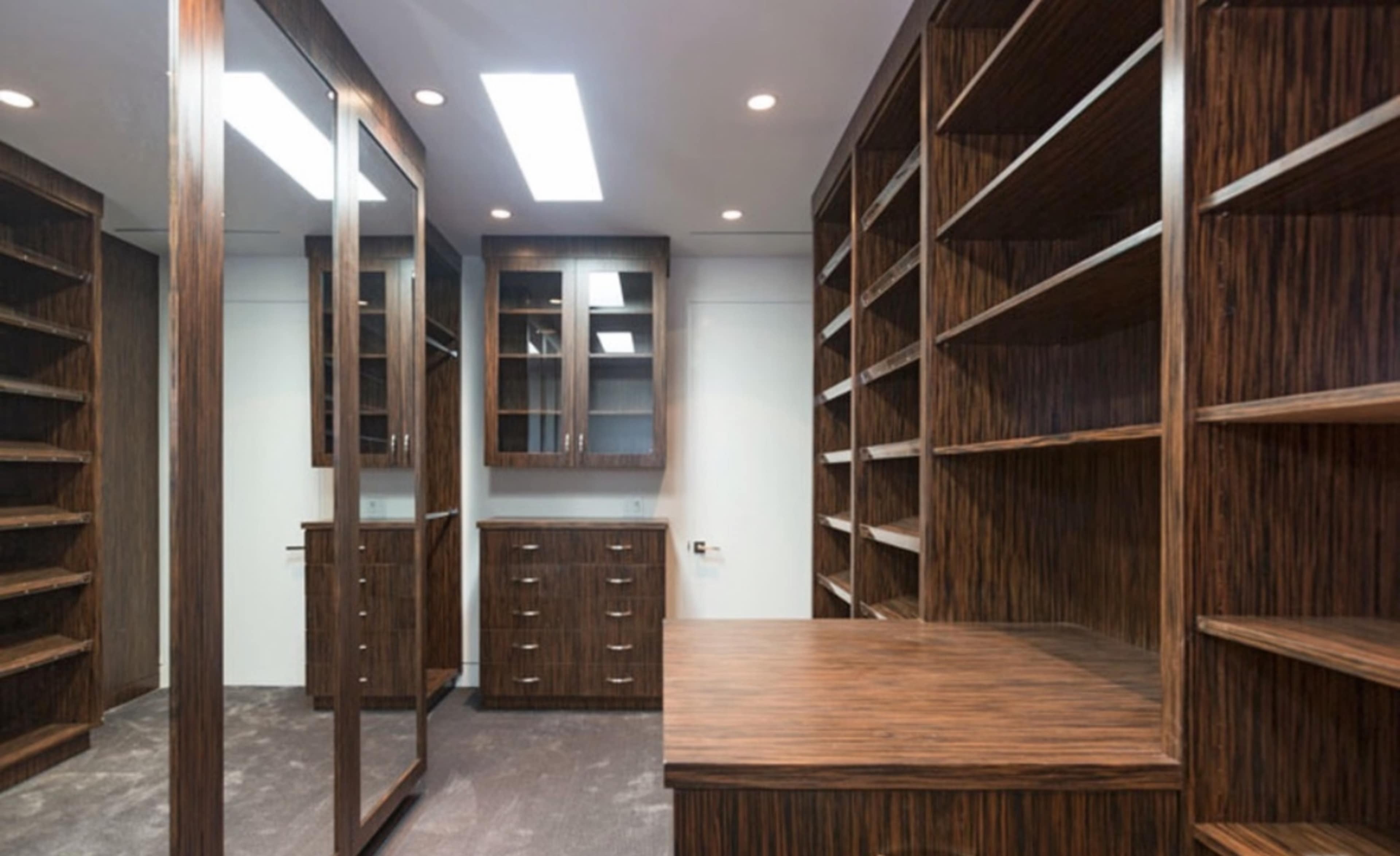 A spacious room with wooden shelves, a large mirror, and a set of drawers against a neutral wall.