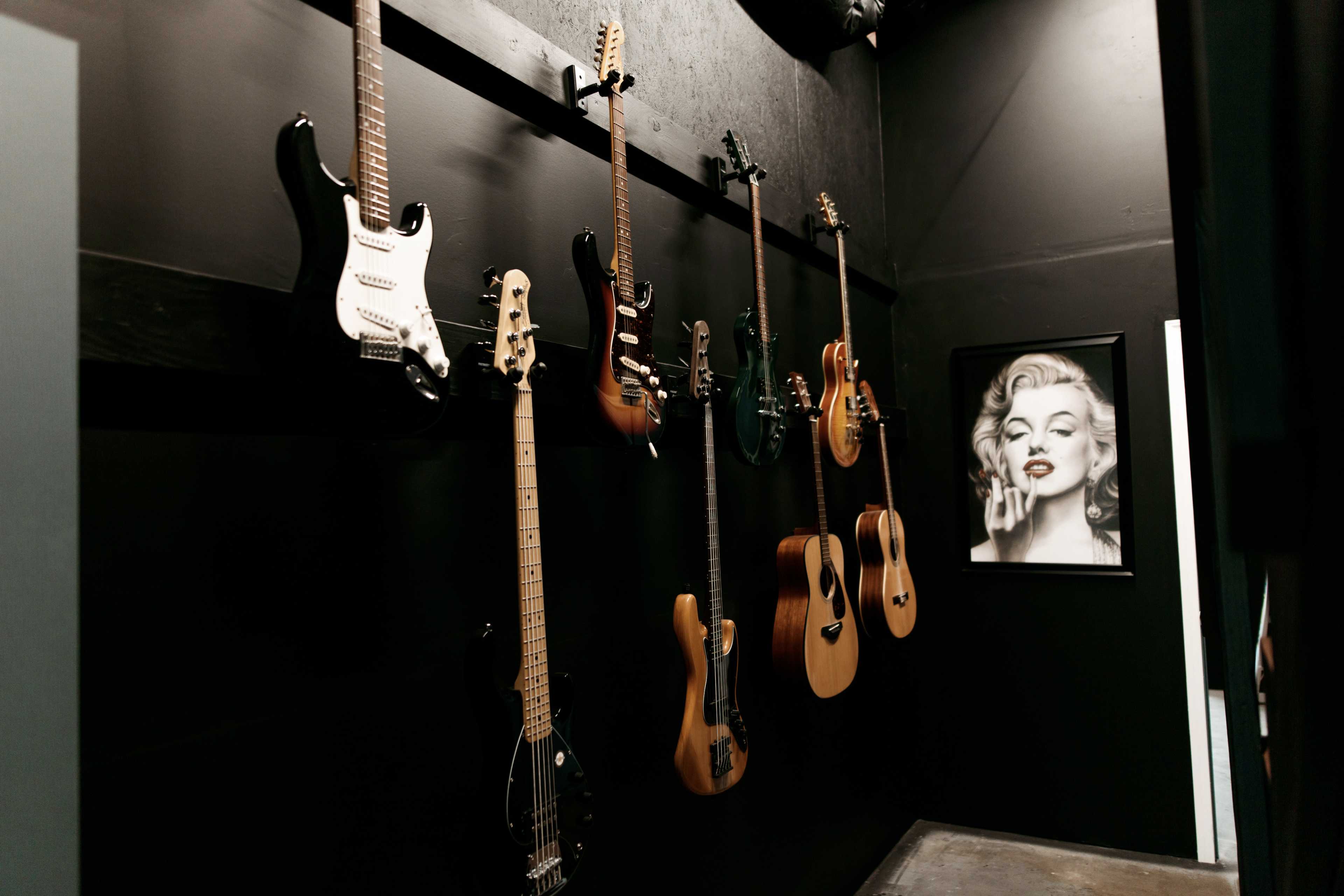 A collection of guitars hangs on a black wall next to a framed portrait of Marilyn Monroe.
