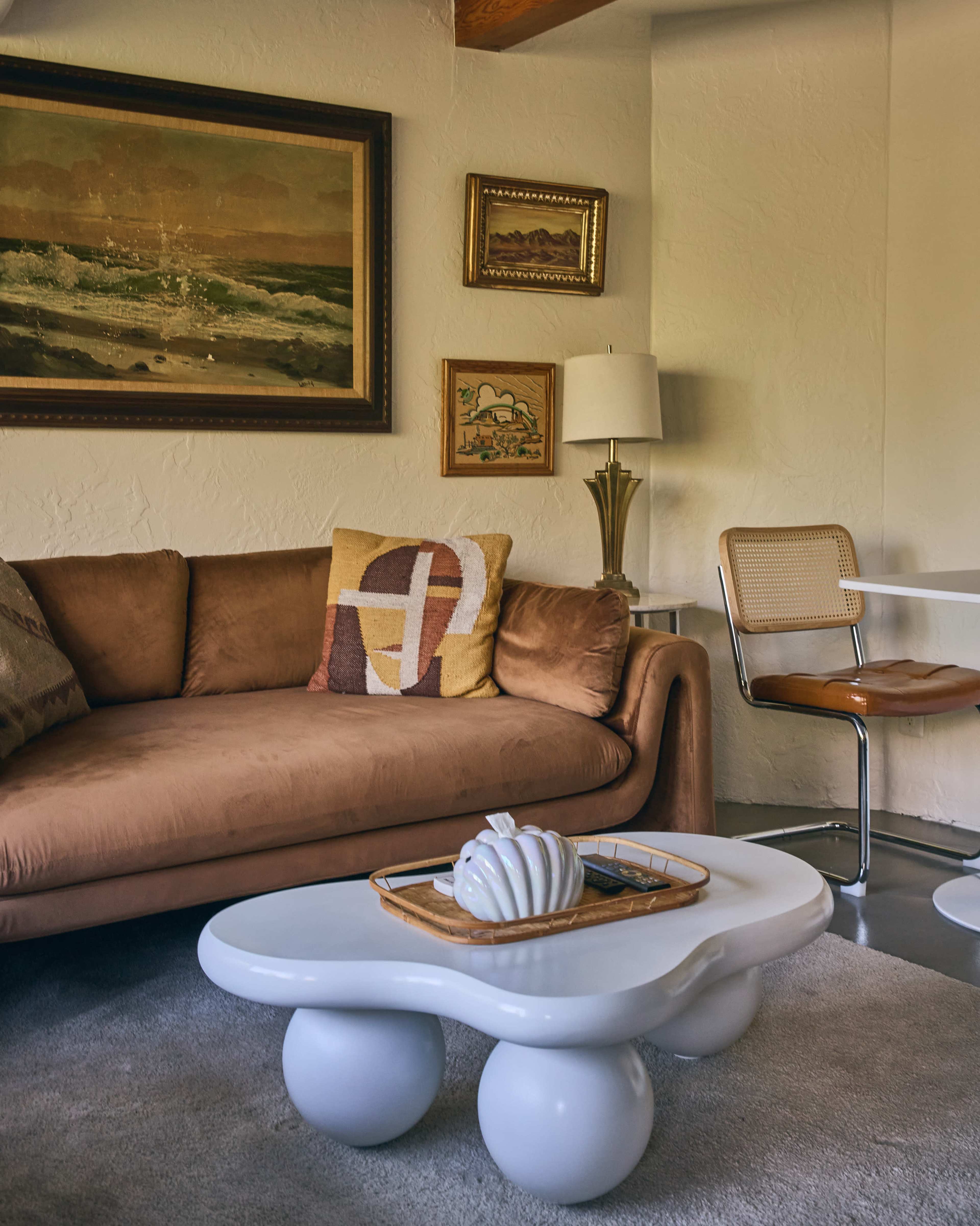 The scene features a cozy living room with a brown sofa, a round coffee table, a lamp, and various framed artworks on the walls.