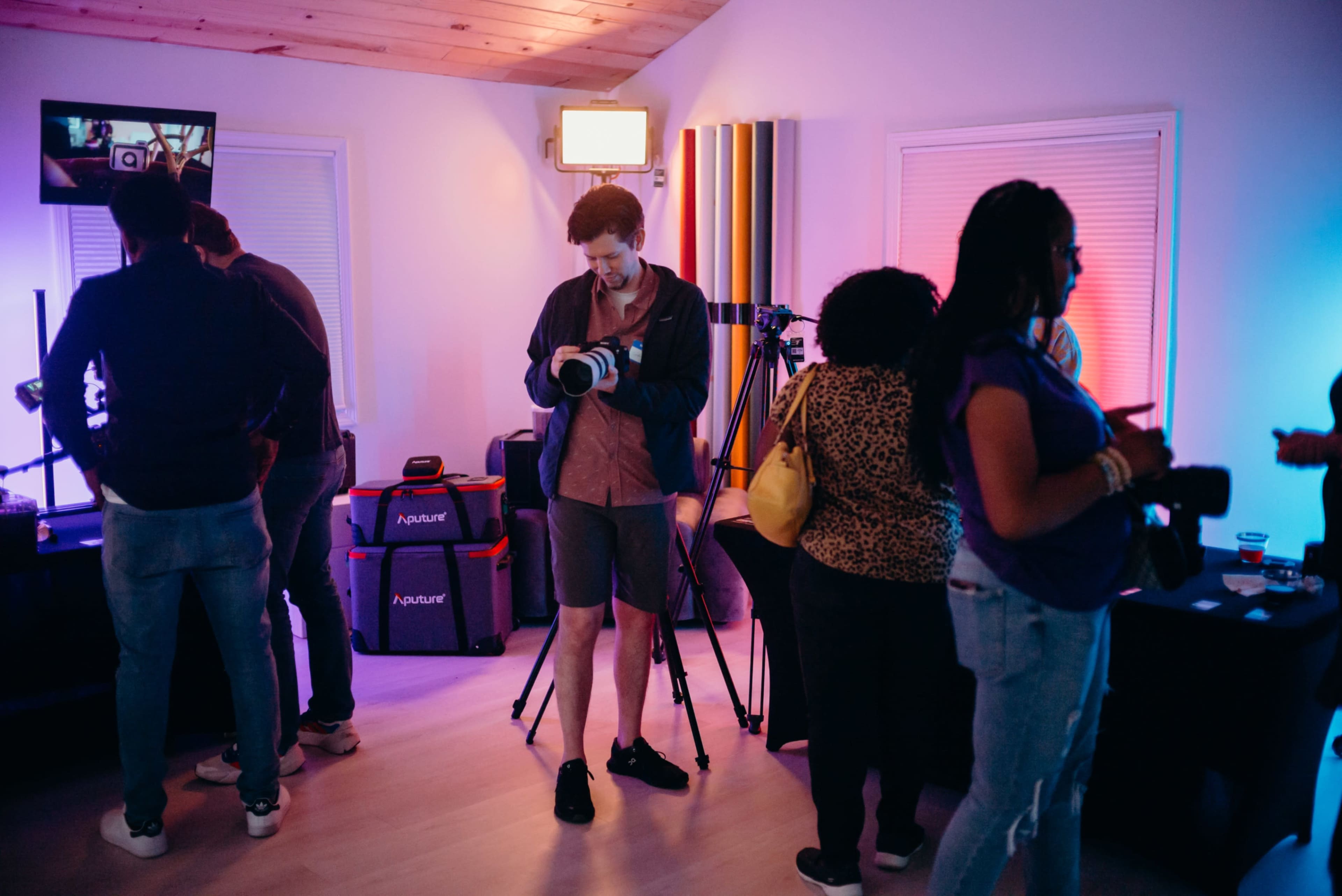 A group of people mingles in a room filled with cameras and colorful ambient lighting, while one man stands with a camera in hand.