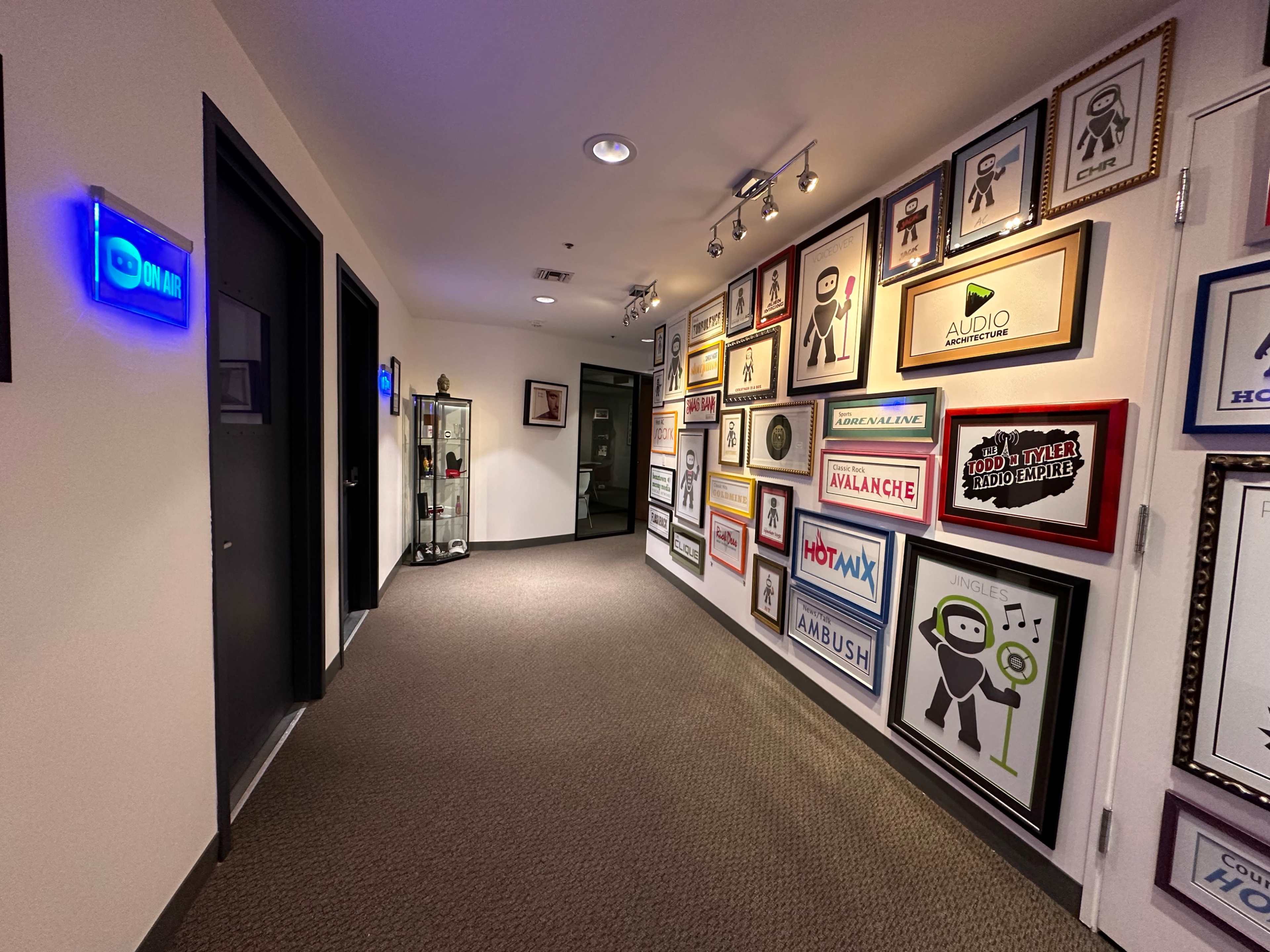 A well-lit hallway lined with framed artwork and signage, leading to black doors on either side.