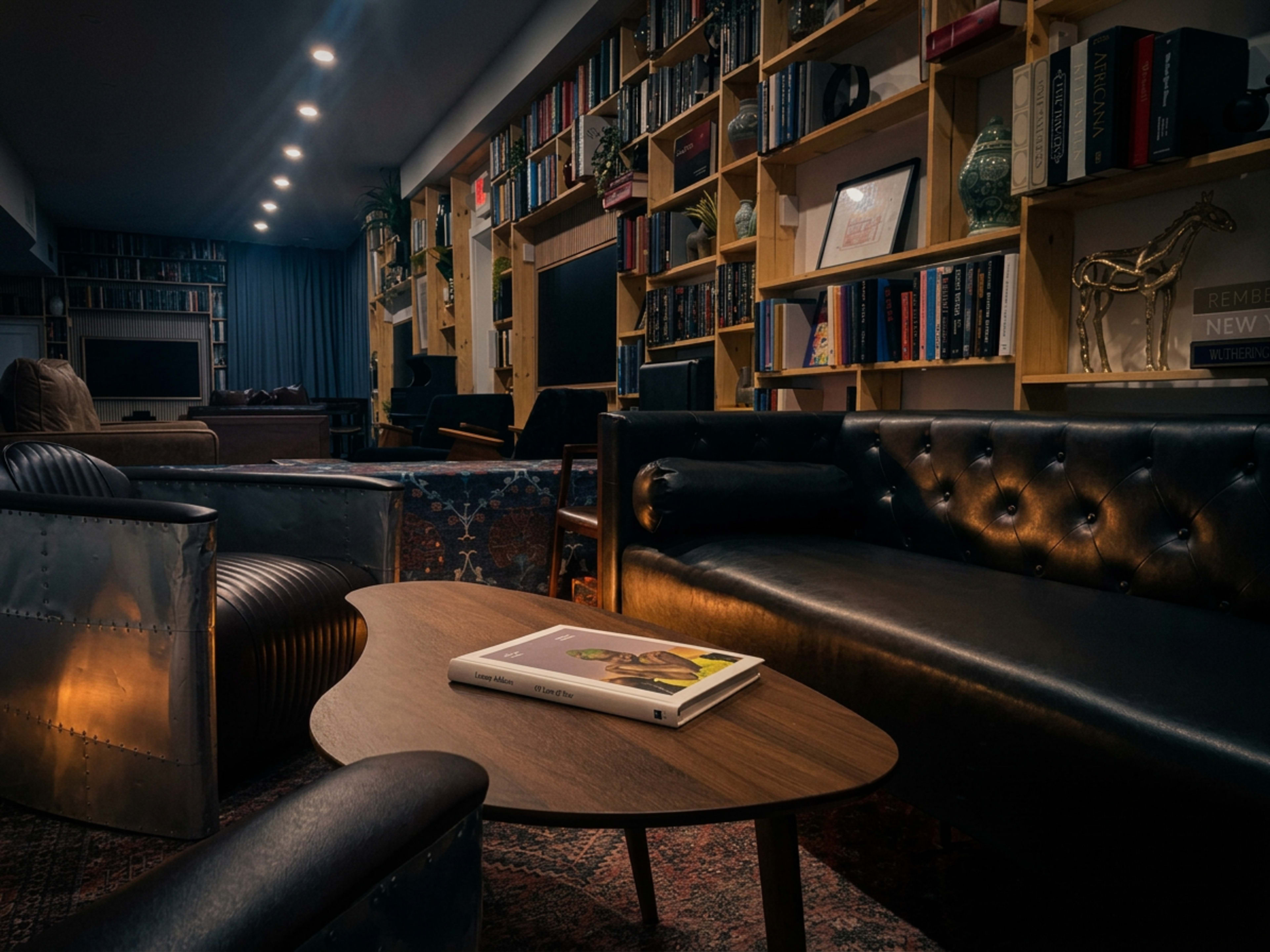The image shows a cozy living room with leather sofas, a coffee table, and bookshelves lined with books.