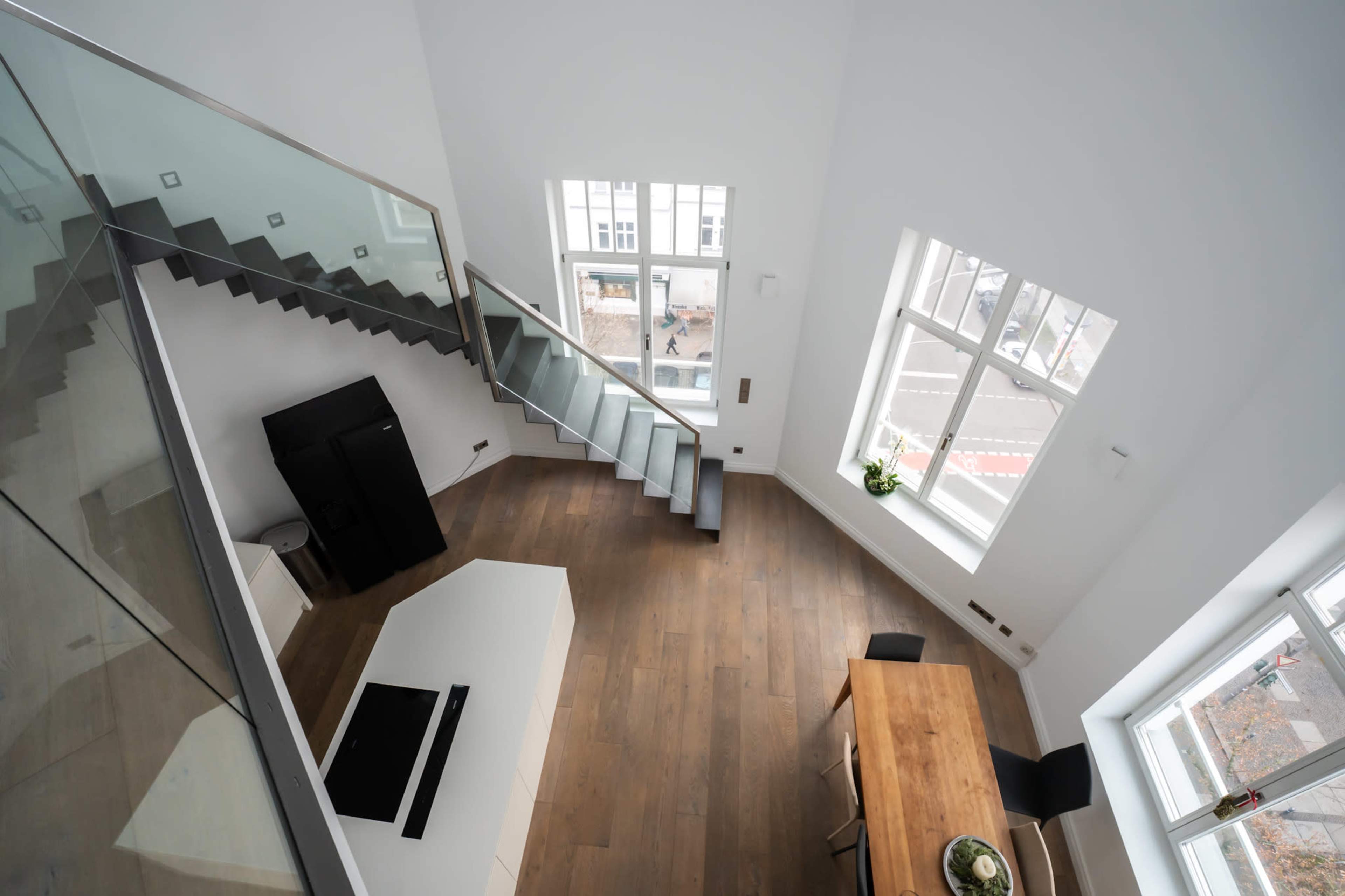 The image shows a modern, open-concept living space featuring a staircase, a dining table, and large windows that provide natural light.