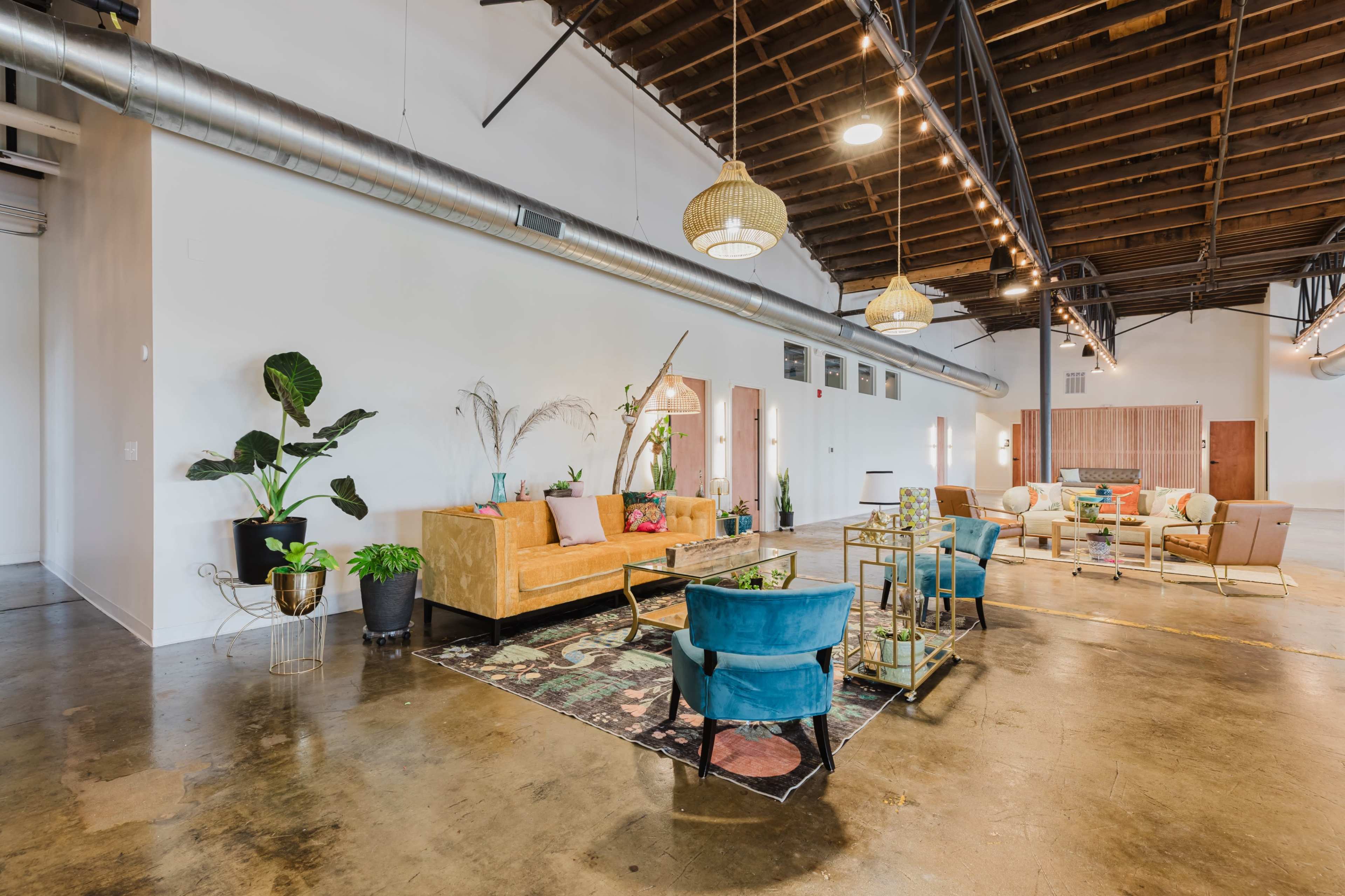 The image showcases a spacious, modern interior with a mix of comfortable seating arrangements, decorative plants, and stylish light fixtures.