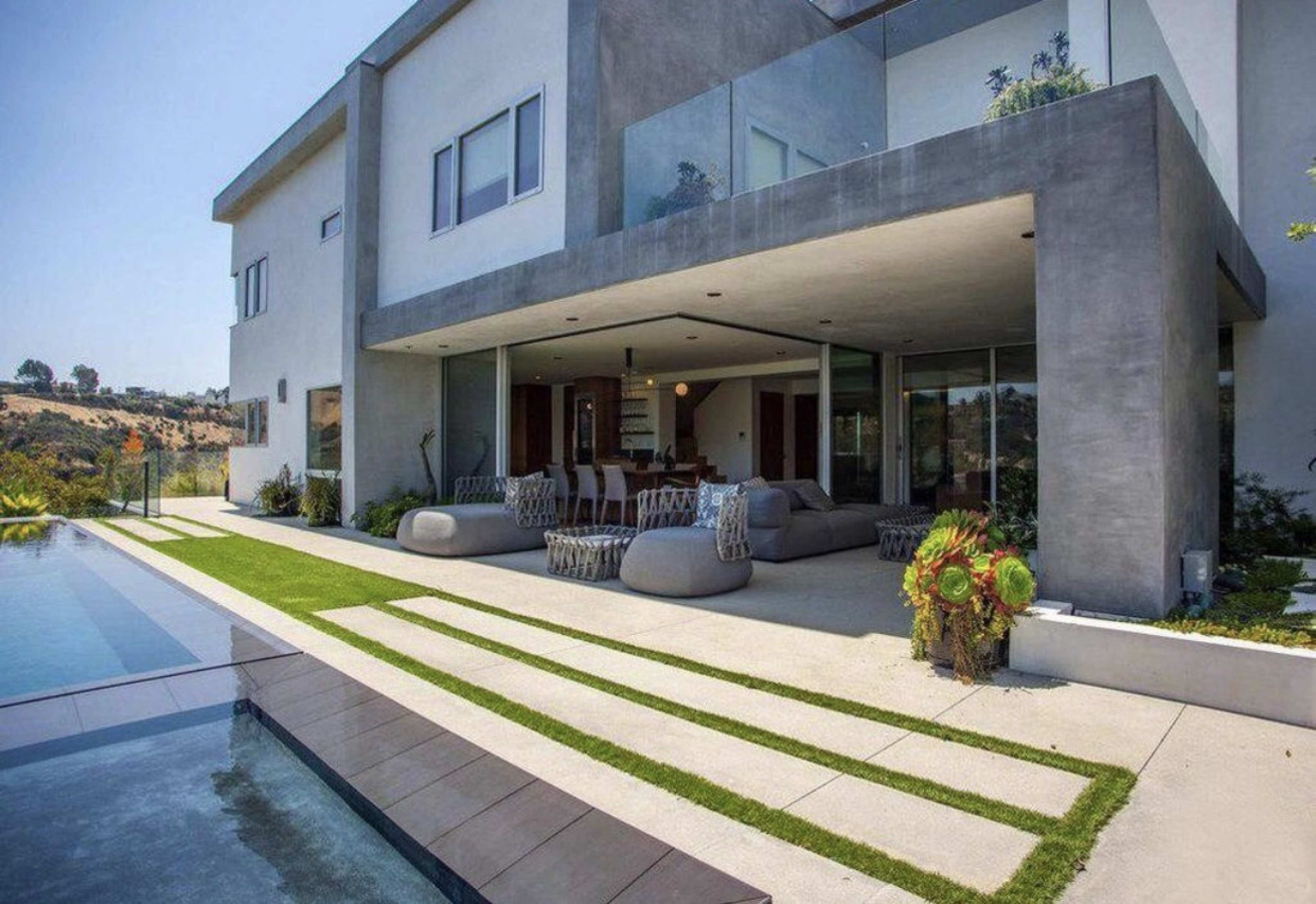 The image shows a modern two-story house with a spacious outdoor patio and a swimming pool.