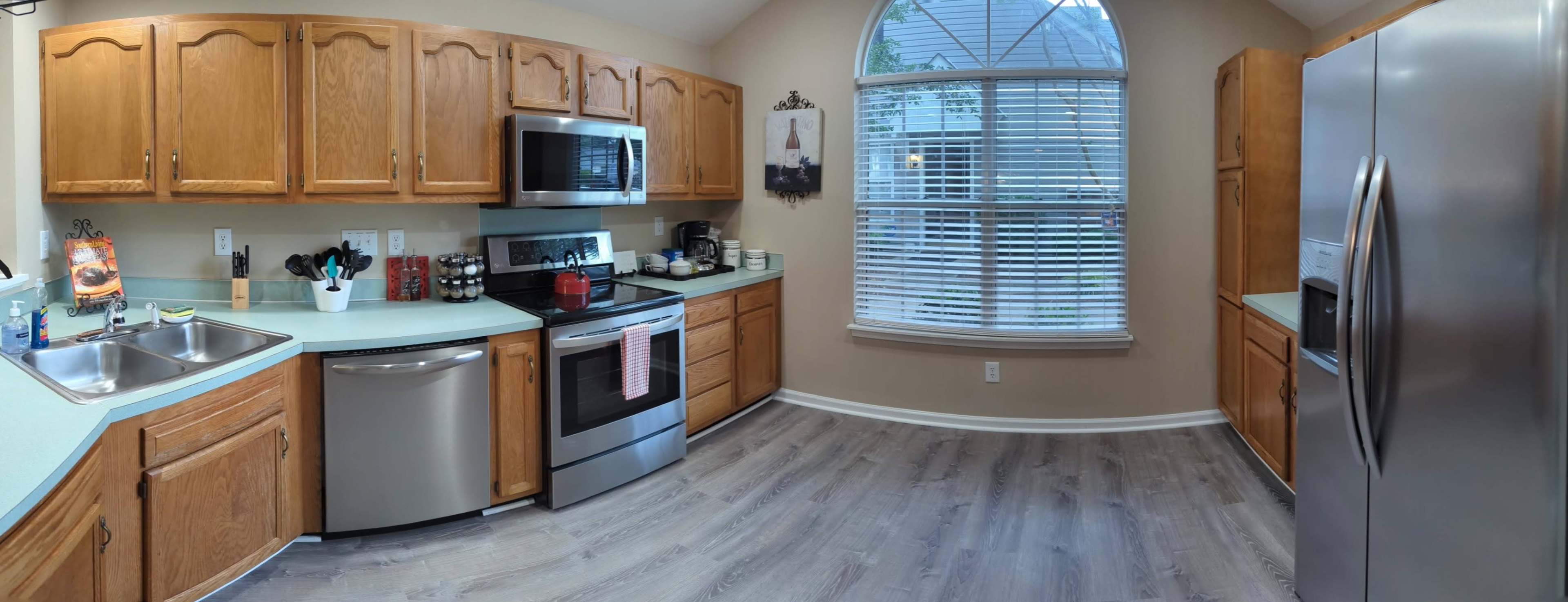 A well-lit kitchen featuring wooden cabinets, stainless steel appliances, and a window with blinds allowing natural light to enter.