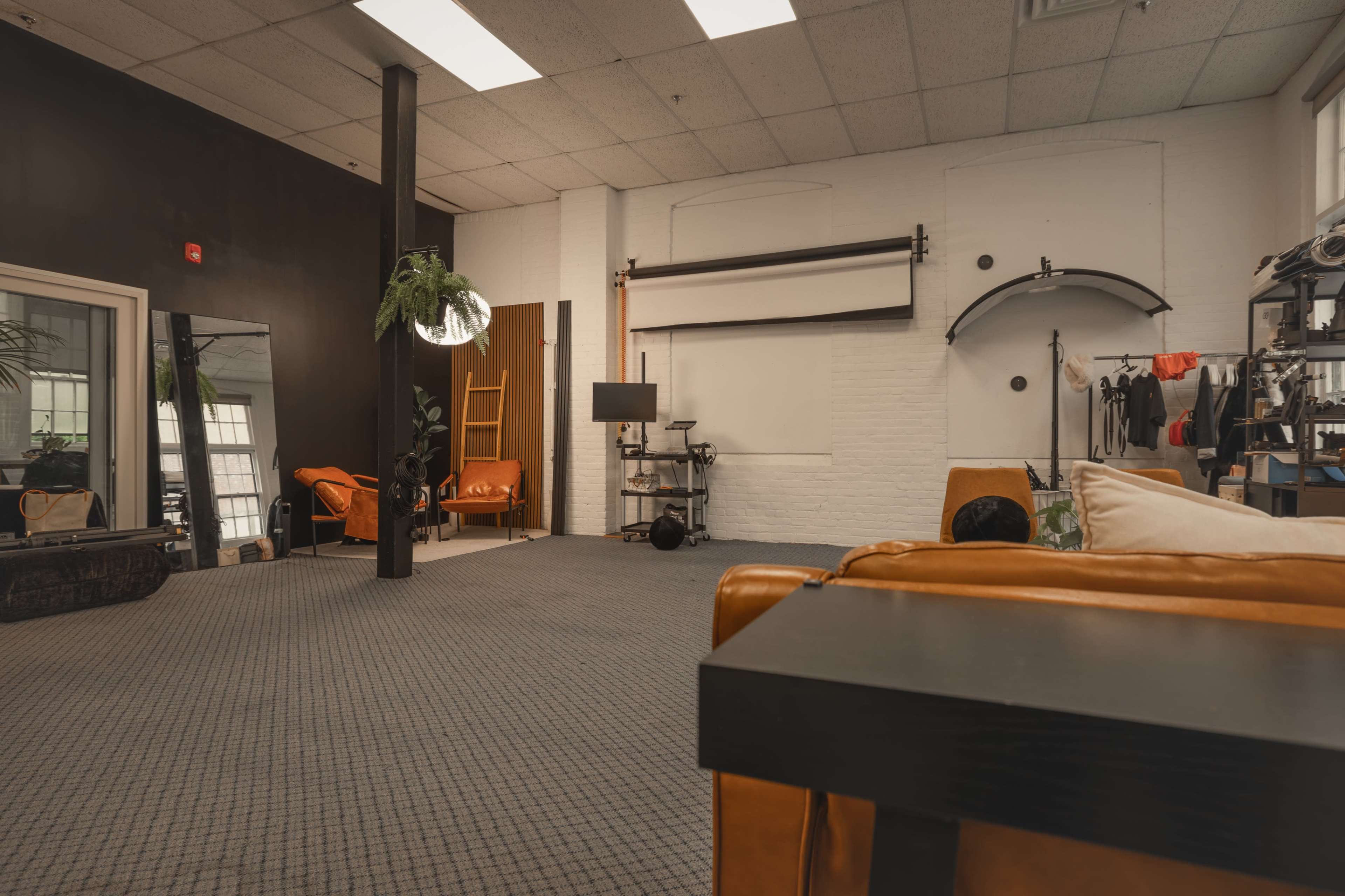 The image shows an indoor space featuring a lounge area with orange couches, a large mirror, and various photography equipment against a brick wall.