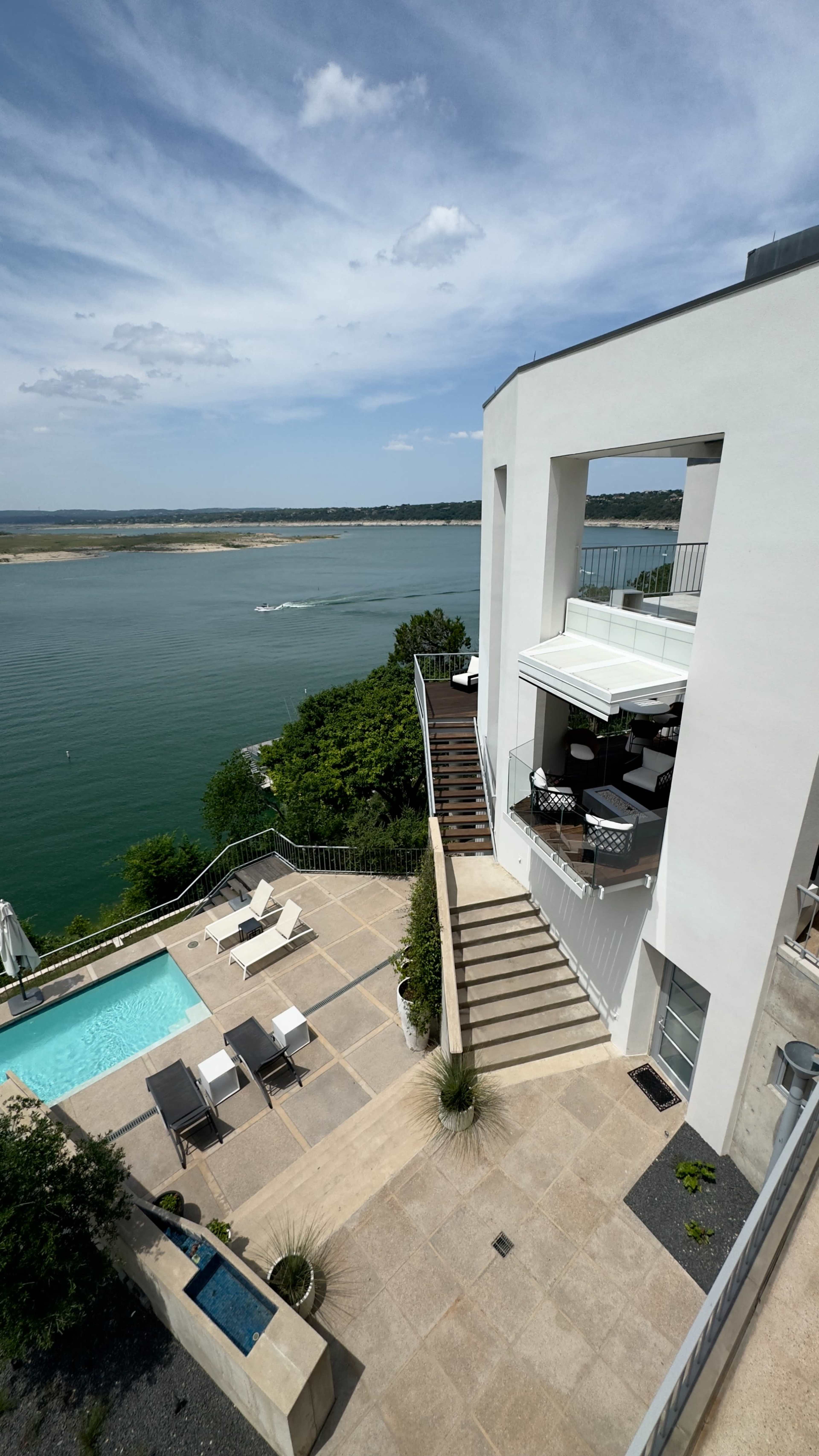 The image shows a modern waterfront home with a terrace that features a swimming pool, overlooking a river and green landscape.