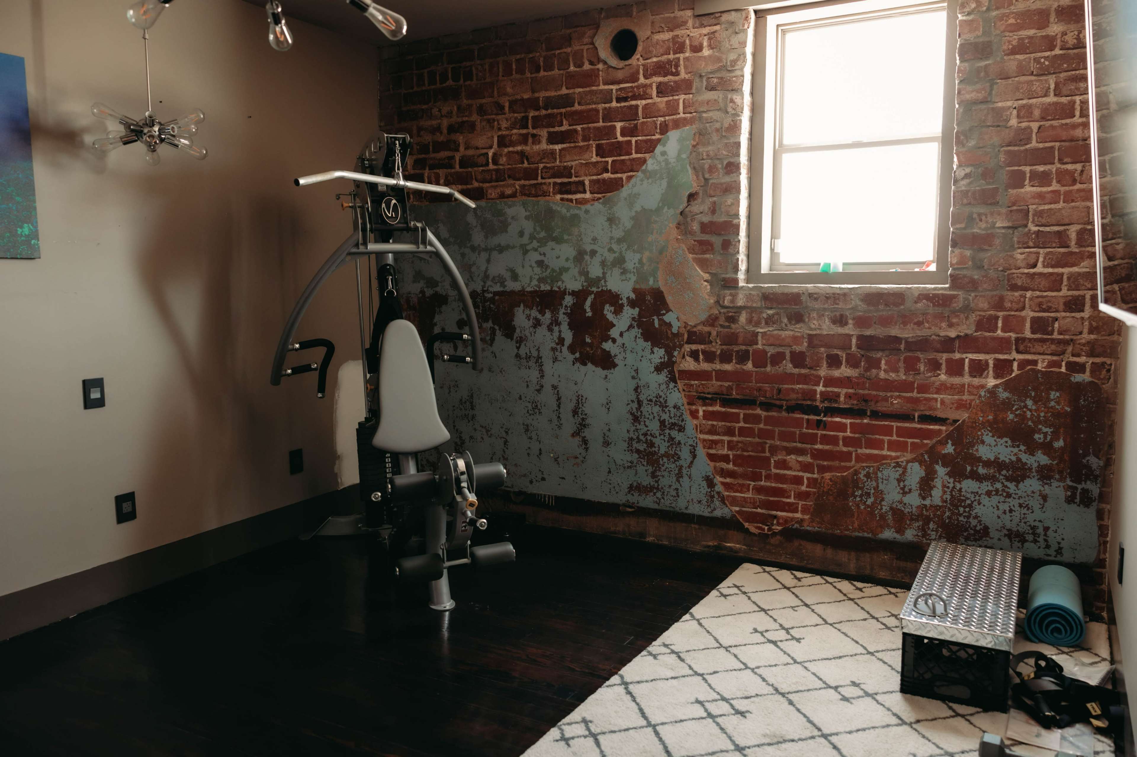 A workout space with a fitness machine, a patterned rug, and a brick wall featuring peeling paint.