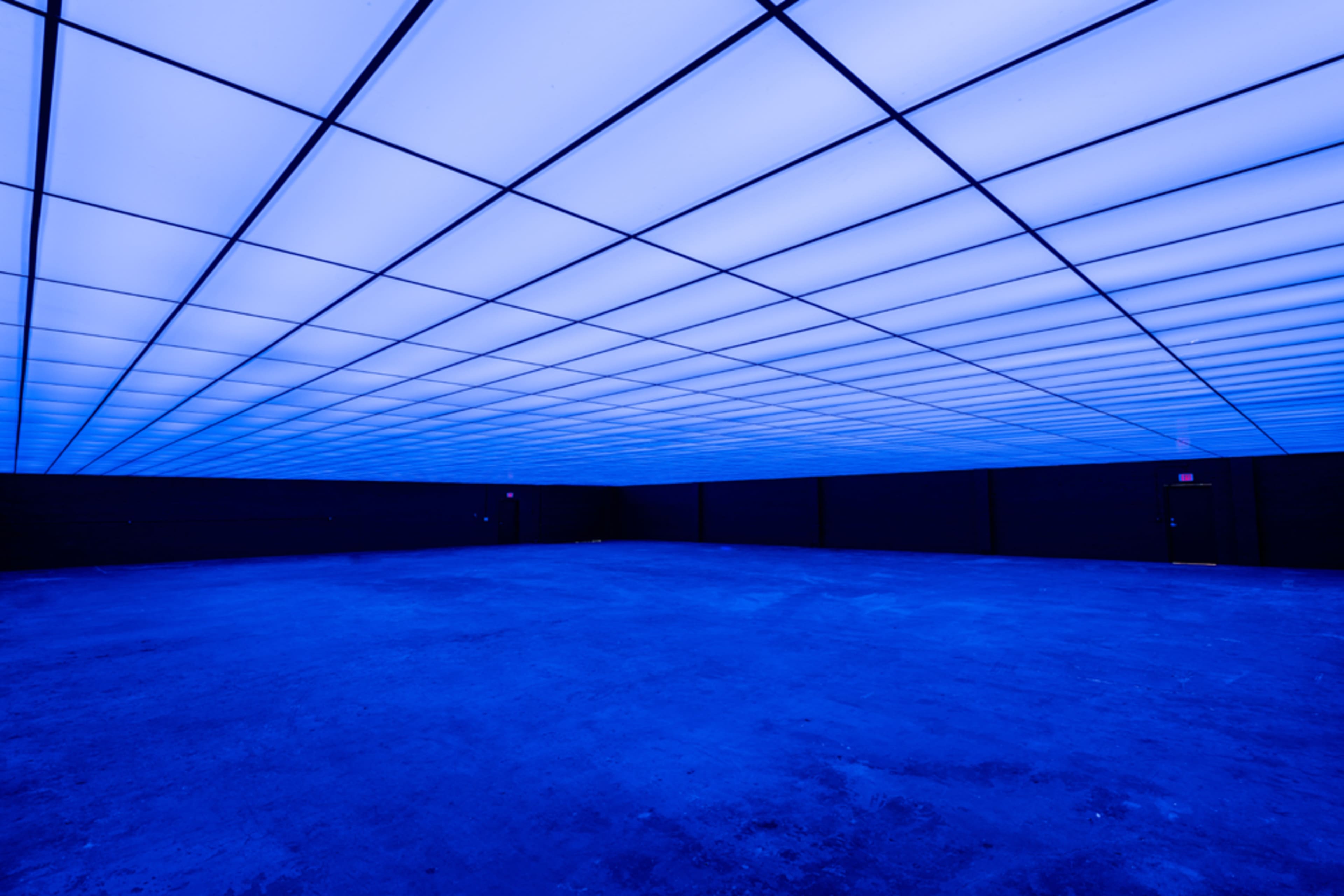 A large, empty room with a blue illuminated ceiling and dark walls.