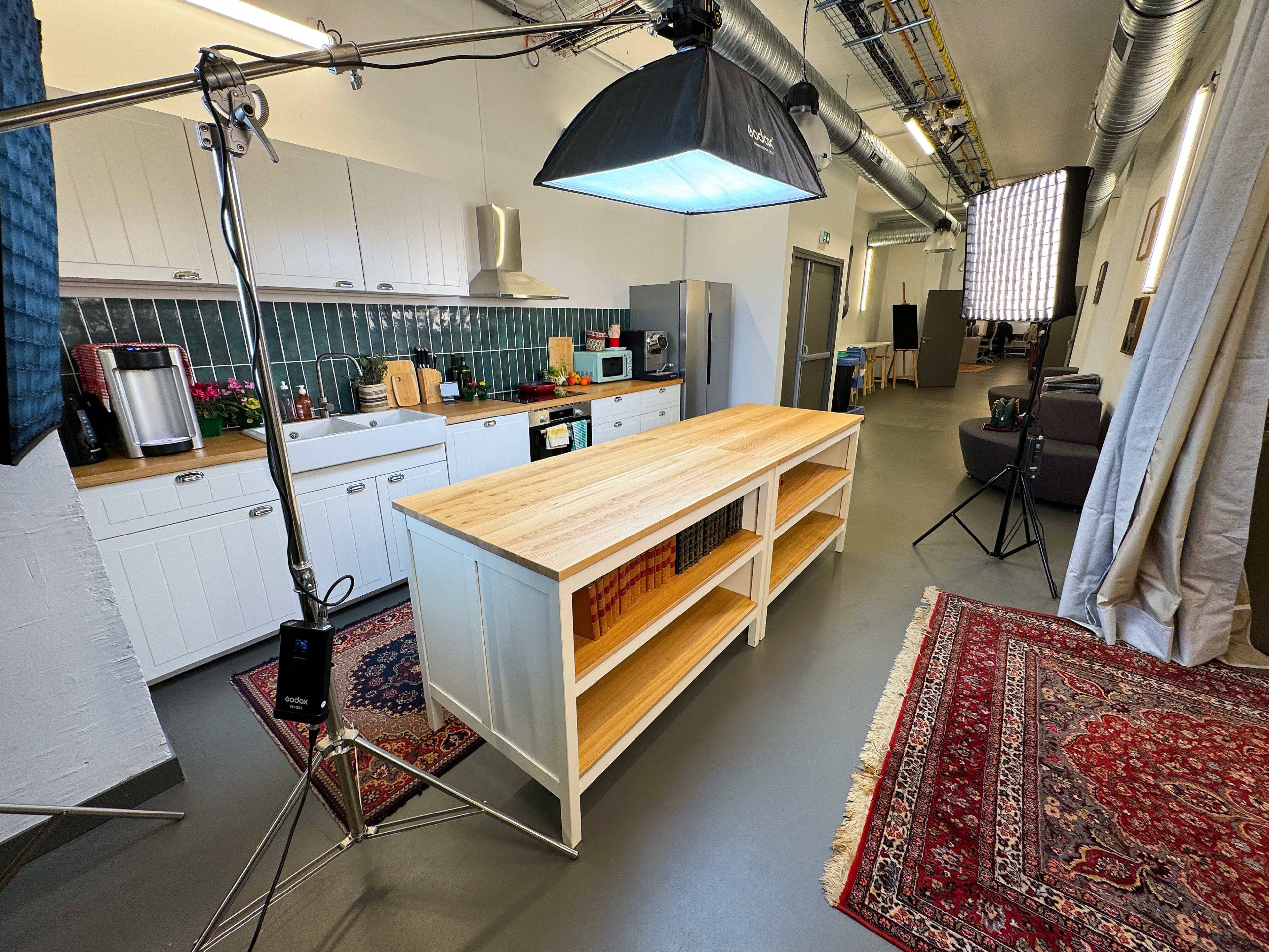 A well-equipped kitchen with a large wooden island, surrounded by various appliances and lighting setup for a photoshoot.
