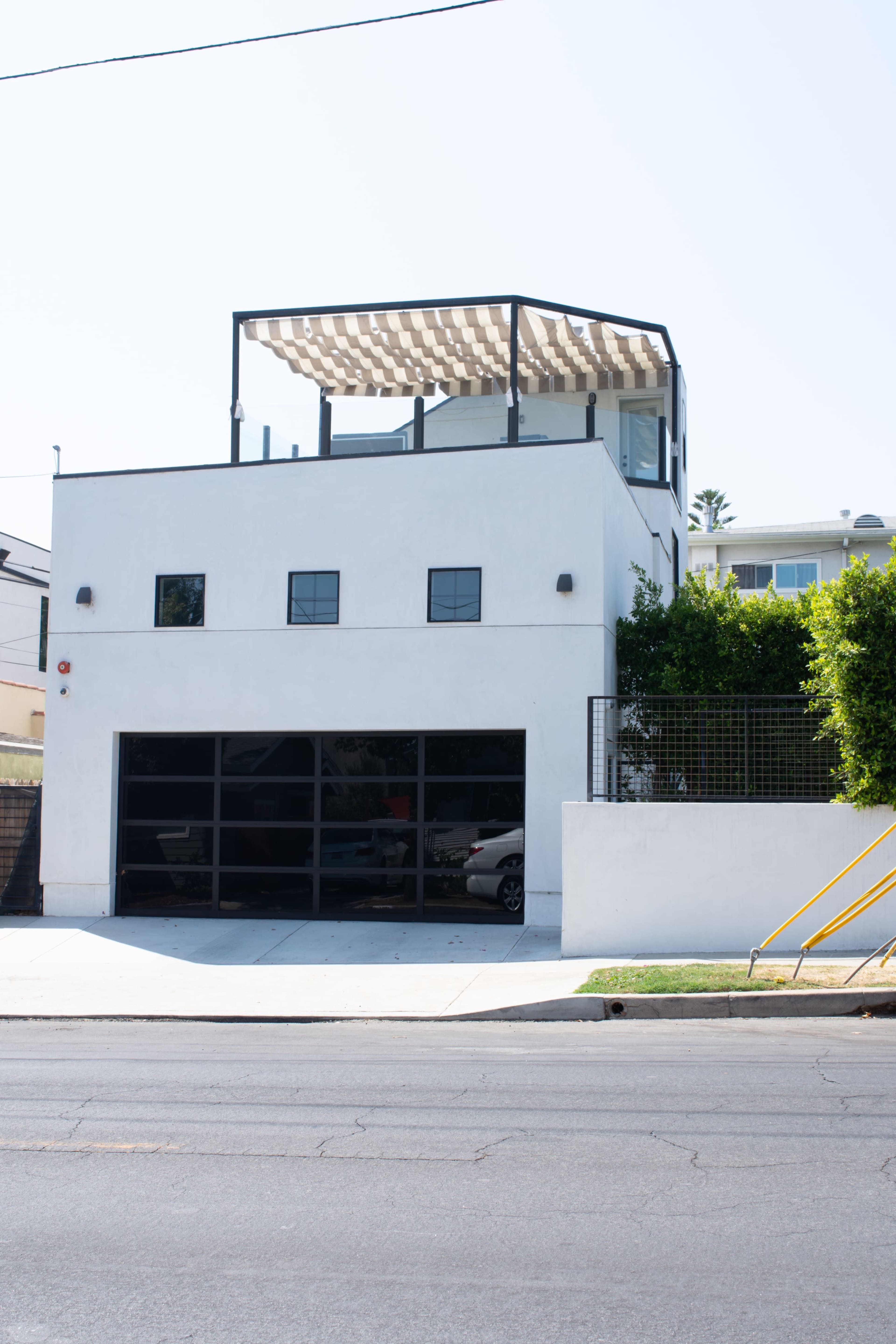A modern, two-story white house with a rooftop patio and a glass garage door.