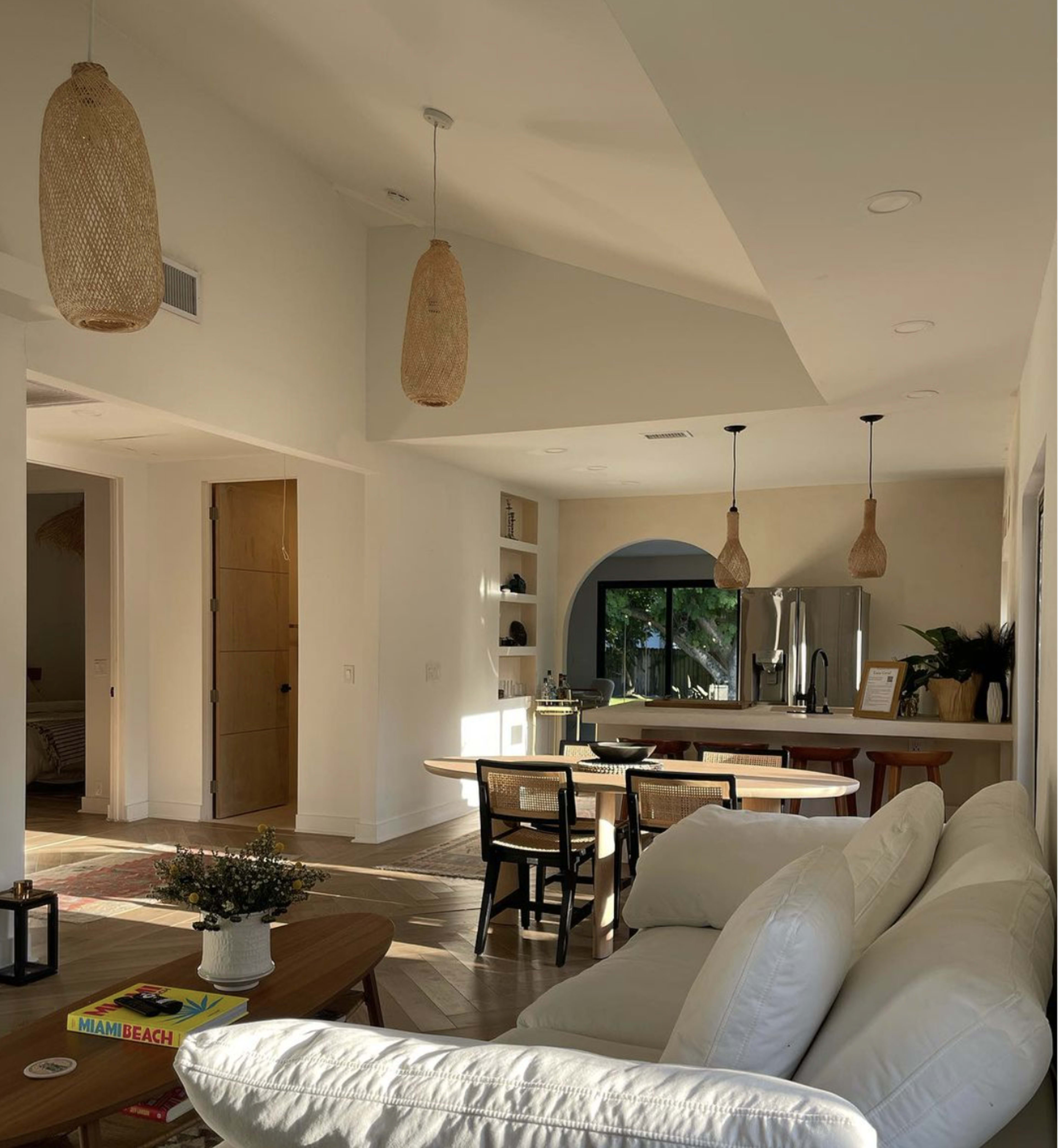 A bright, modern living space with a white sofa, a dining area, and pendant lights hanging from the ceiling.