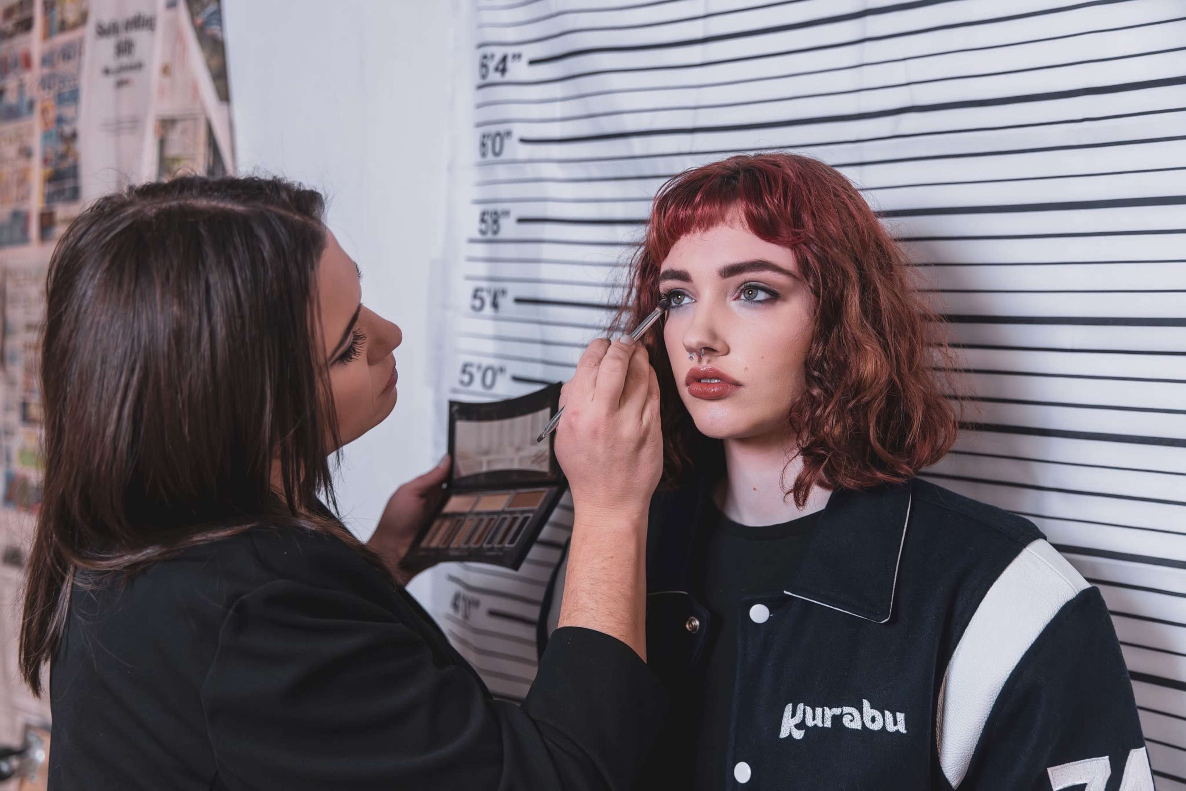 A makeup artist is applying makeup to a model in front of a height chart.