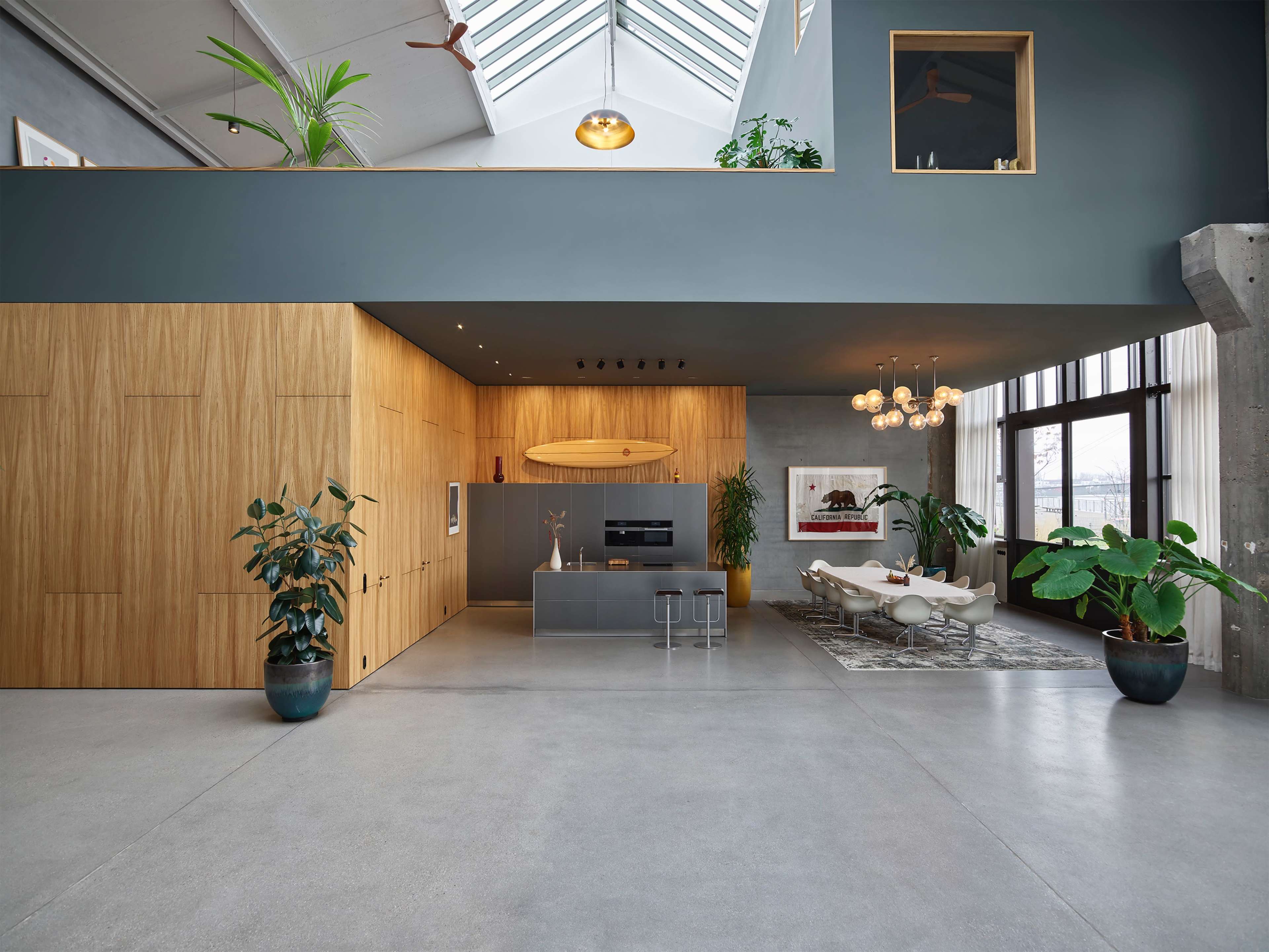 A spacious, modern interior with high ceilings, wooden cabinetry, a kitchen area, and a dining space furnished with stylish chairs and plants.