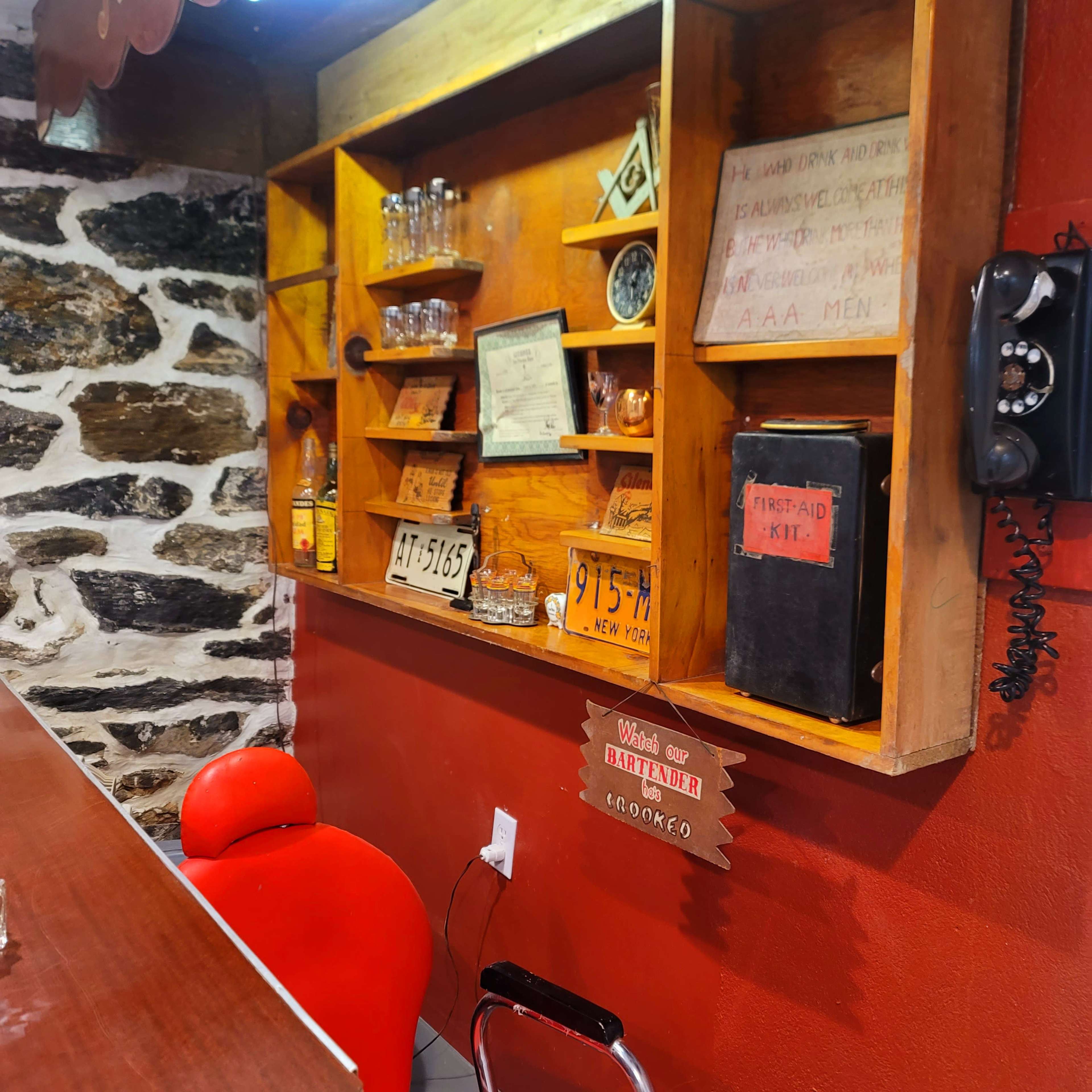 A wooden shelf displaying various items, including glassware and vintage signs, against a stone wall in a dimly lit space with a red accent.