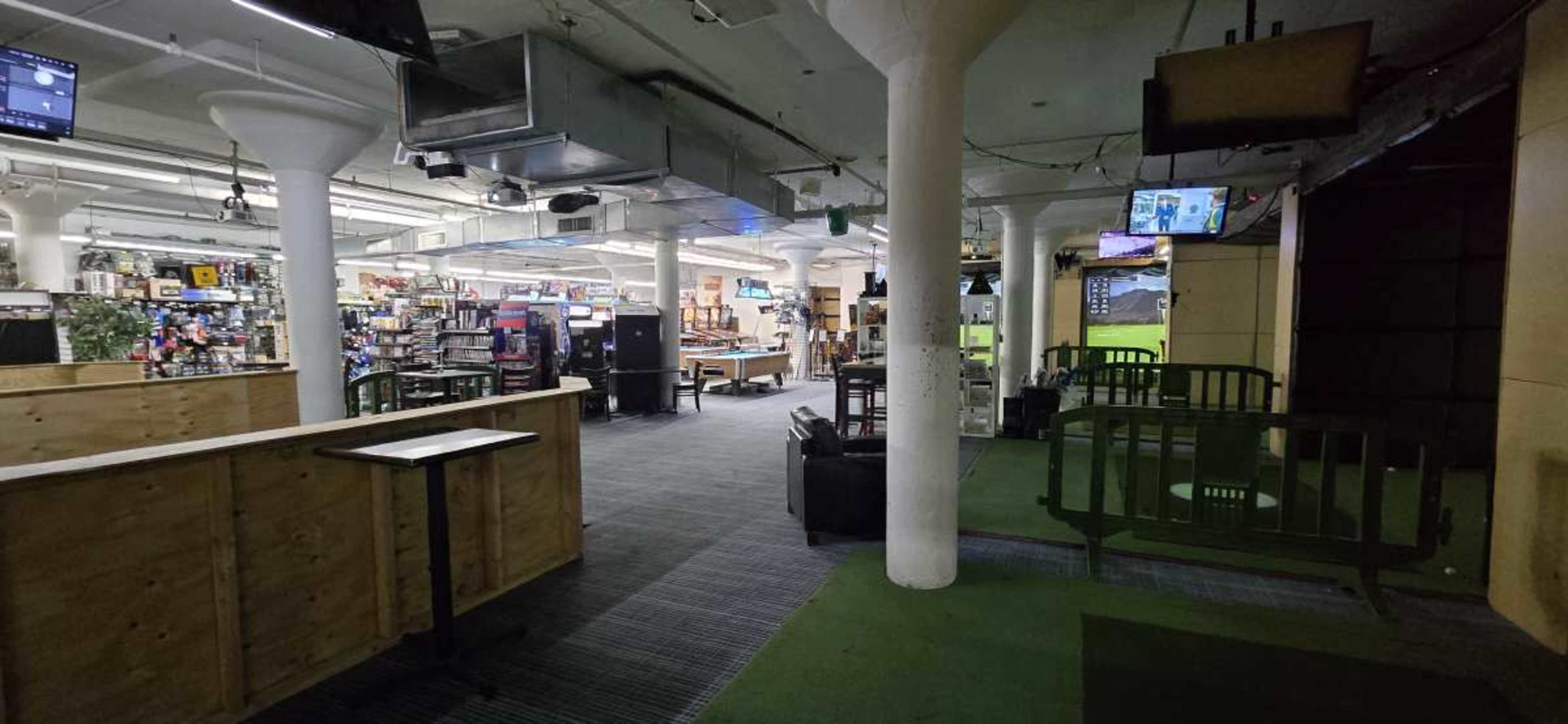 The image shows an indoor retail space with rows of shelves displaying merchandise, tables, and seating areas, all under a well-lit ceiling with visible columns.