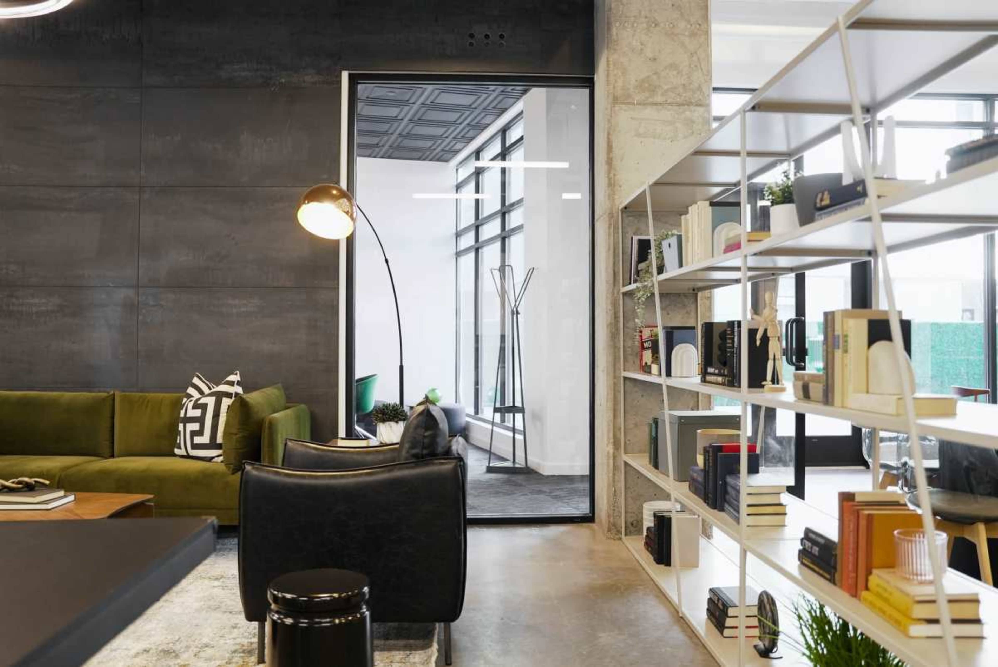 A modern office space featuring a green sofa, a bookshelf filled with books and decorative items, and a doorway leading to another area.