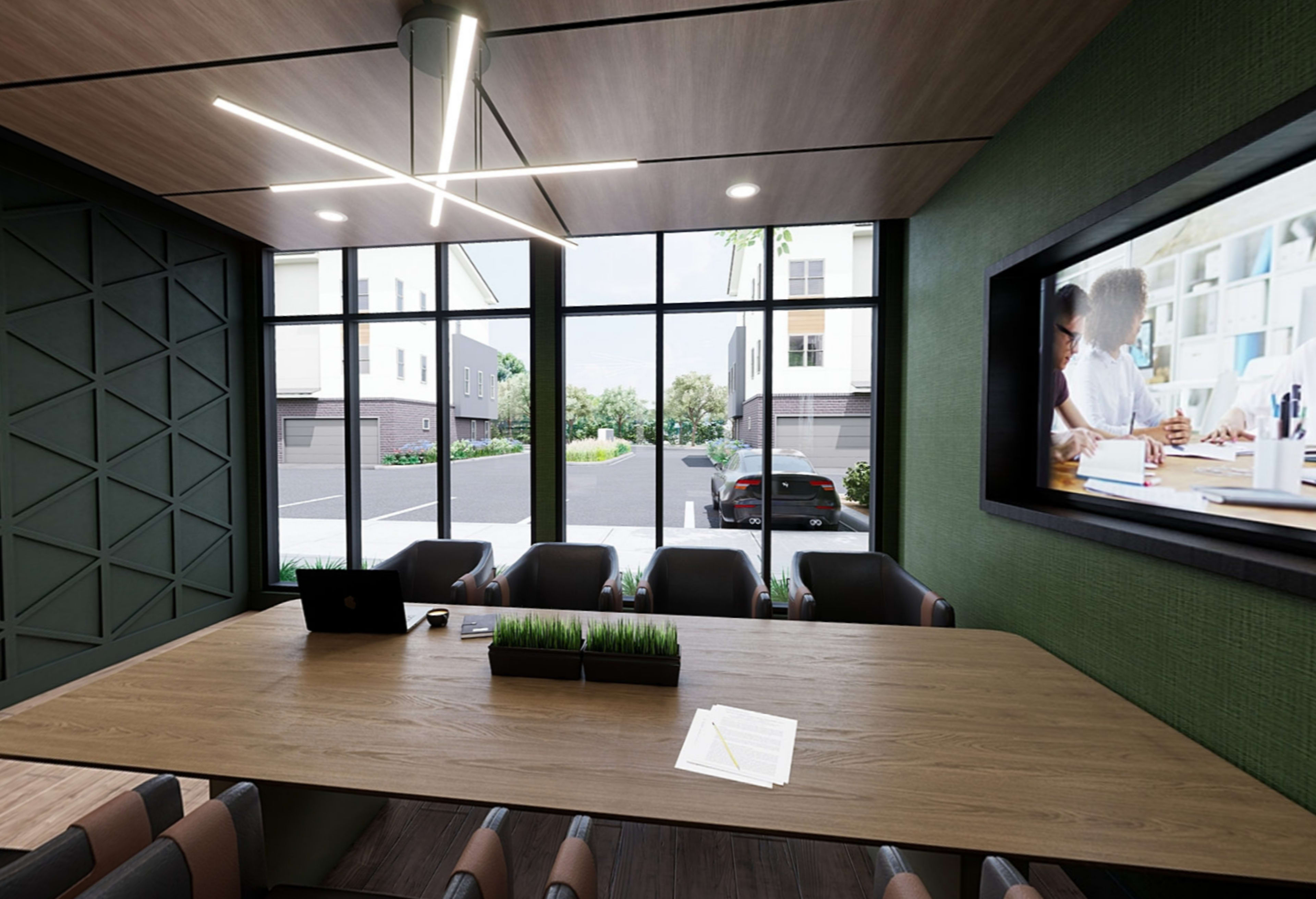 A modern conference room features a large wooden table, comfortable chairs, and large windows overlooking a landscaped area and parked cars.