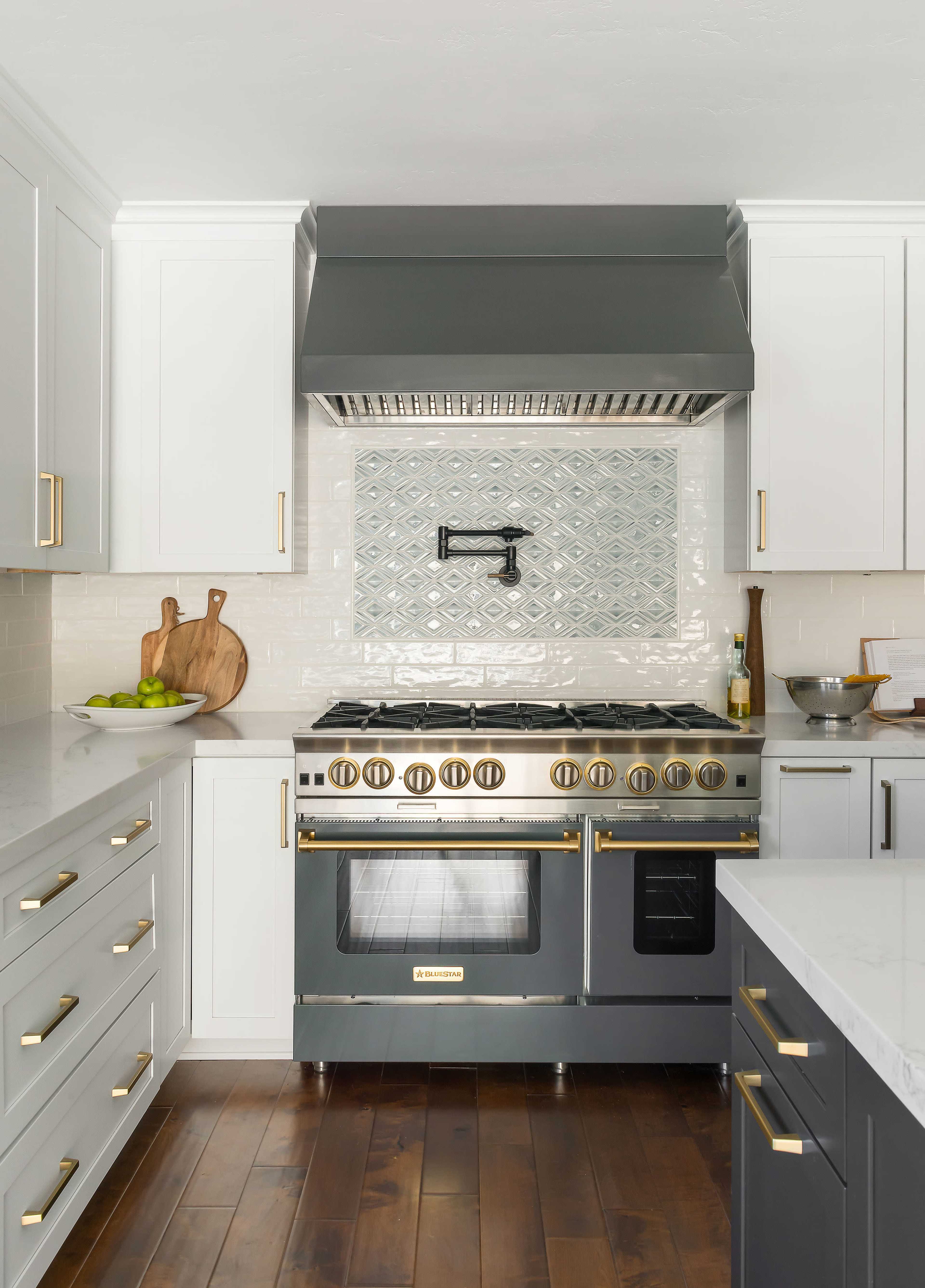 The image shows a modern kitchen with a large gray stove, white cabinetry, and a patterned backsplash.